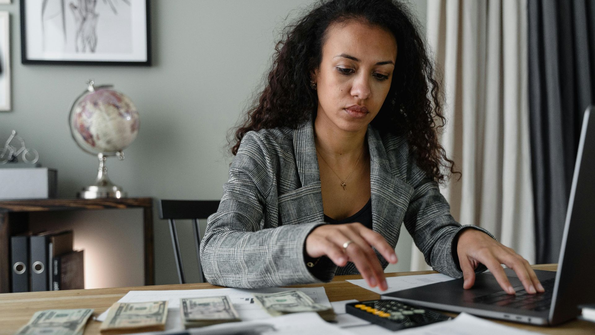 Professional woman analyzing financial documents and counting cash at office desk.