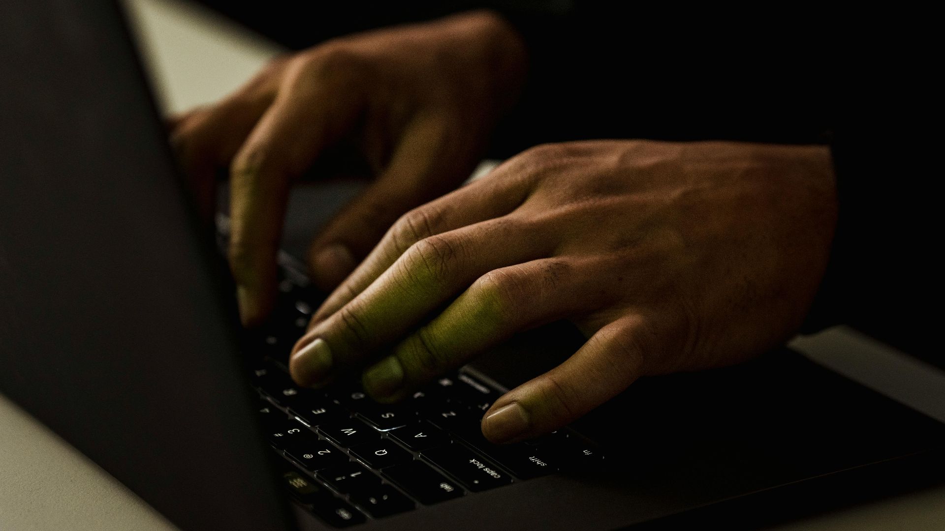 A close-up view of hands typing on a laptop keyboard in a dimly lit environment.