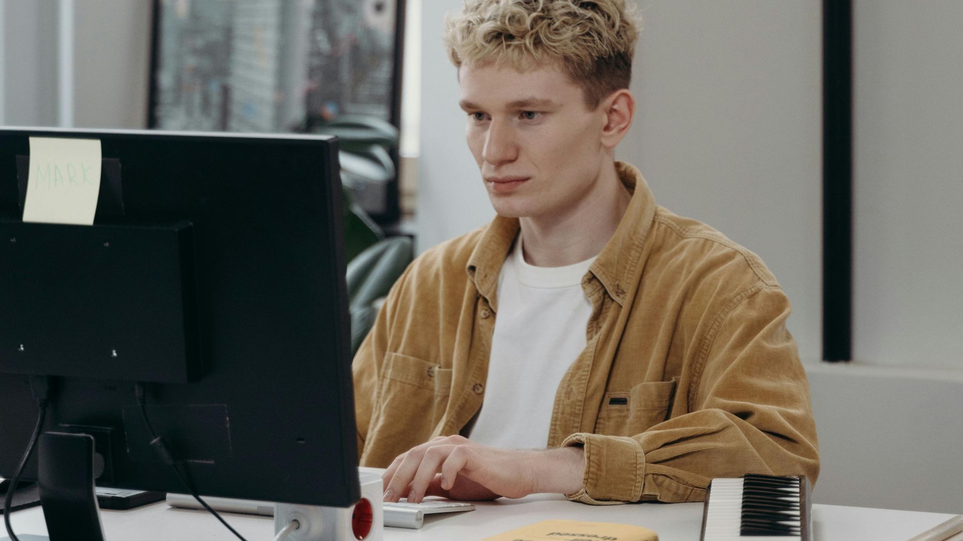 A young man working at a computer in a modern office setting, focused on a project.
