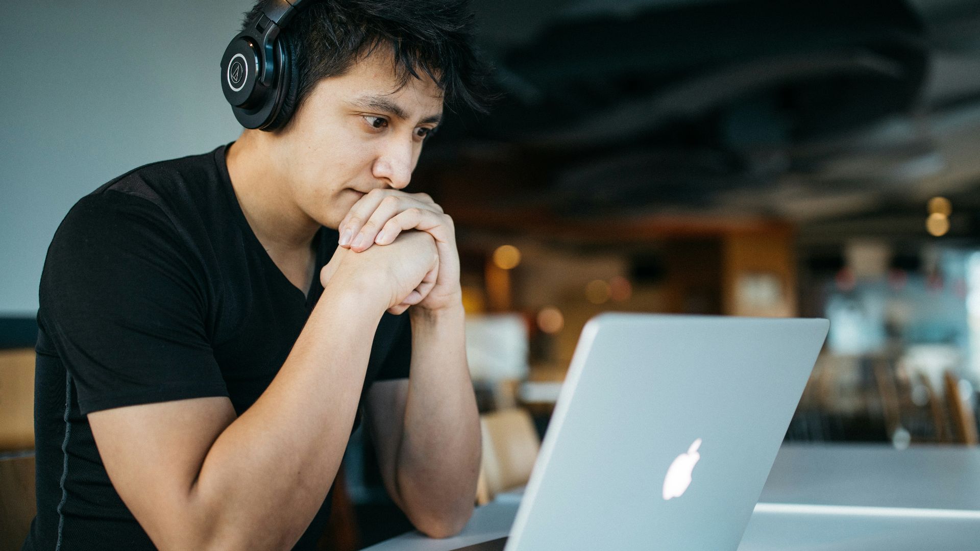 man wearing headphones while sitting on chair in front of MacBook