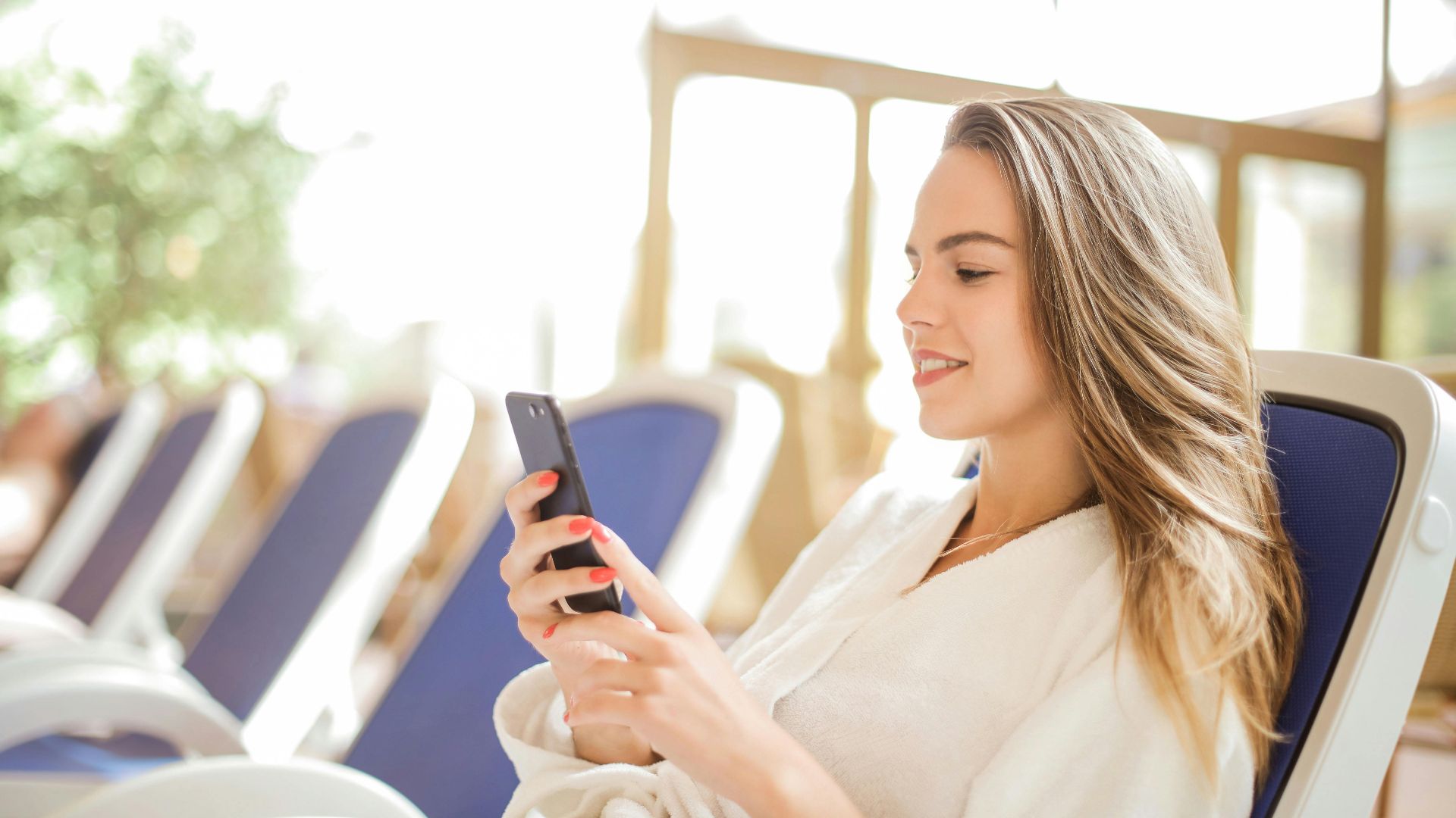 Young woman in bathrobe using smartphone, enjoying leisure time in a comfortable setting.