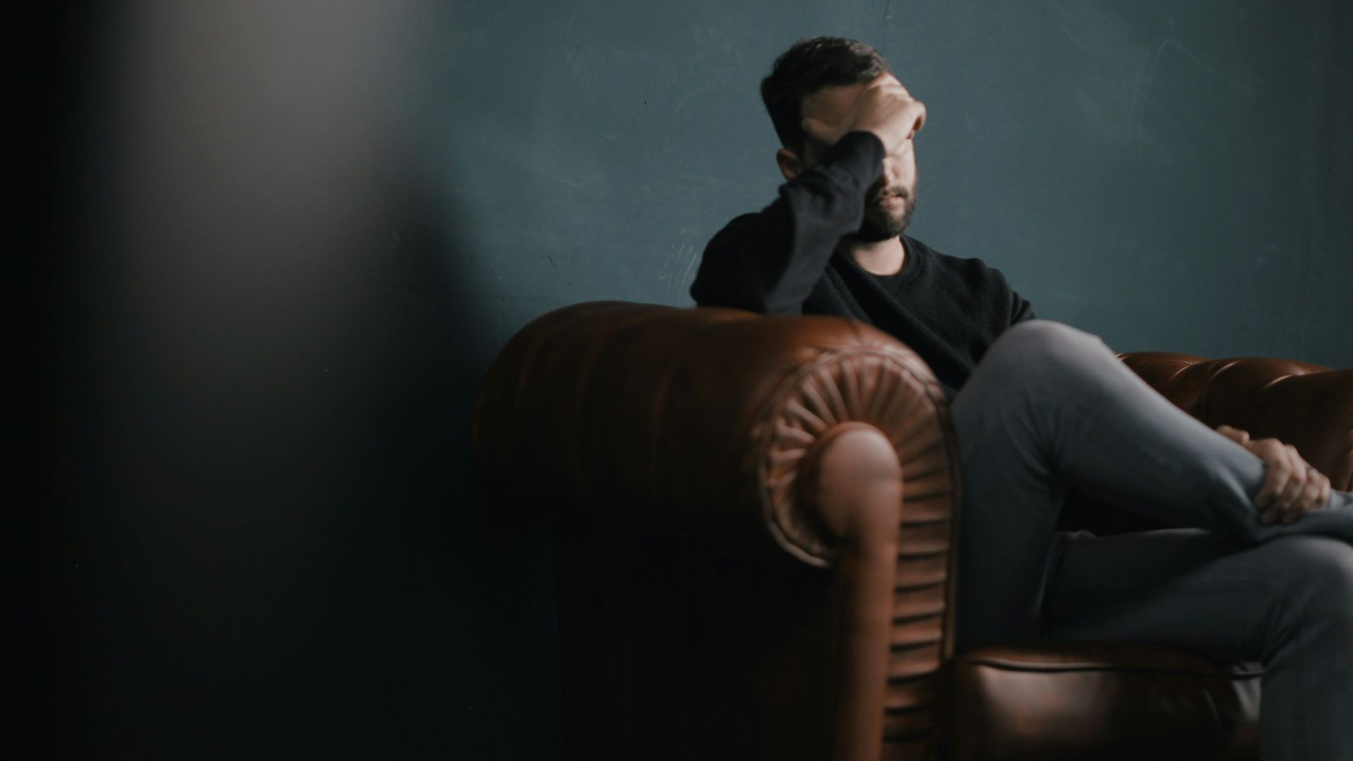 a man holds his head while sitting on a sofa
