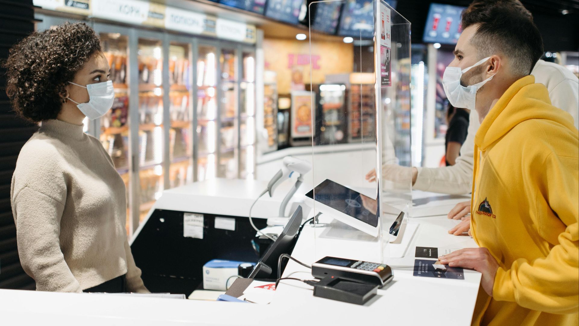 People in masks interacting at a cinema counter, highlighting the new normal during COVID-19.