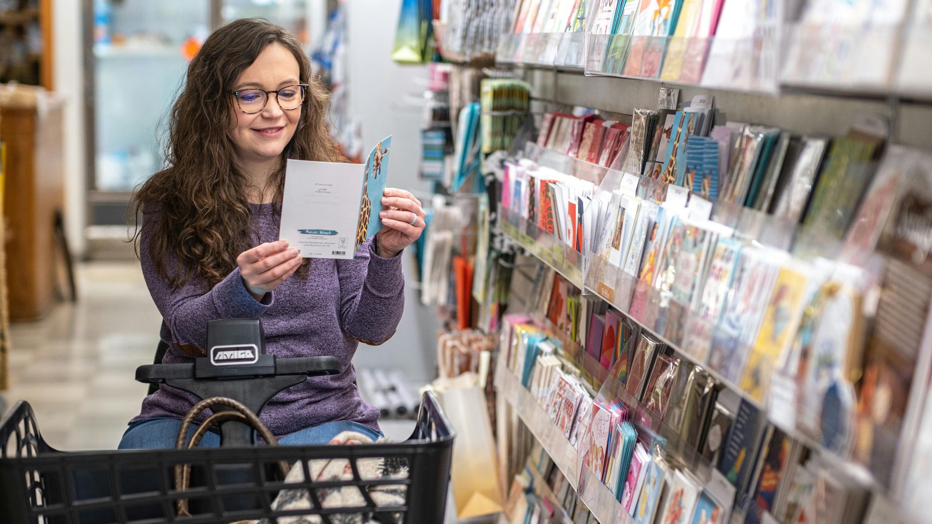 A woman carefully selects a greeting card from a store display.