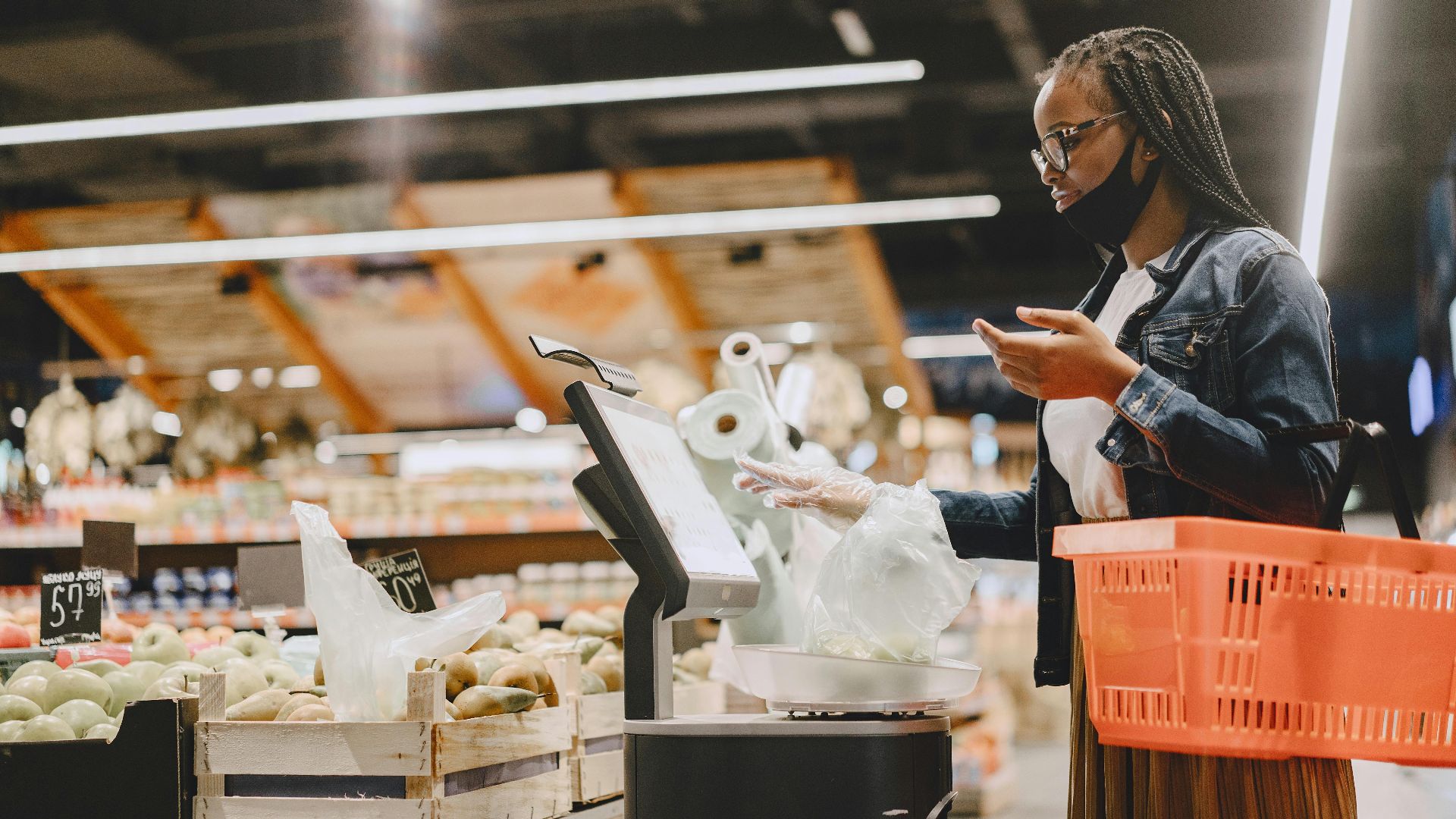 A woman with a mask shops and weighs groceries in a modern supermarket setting.