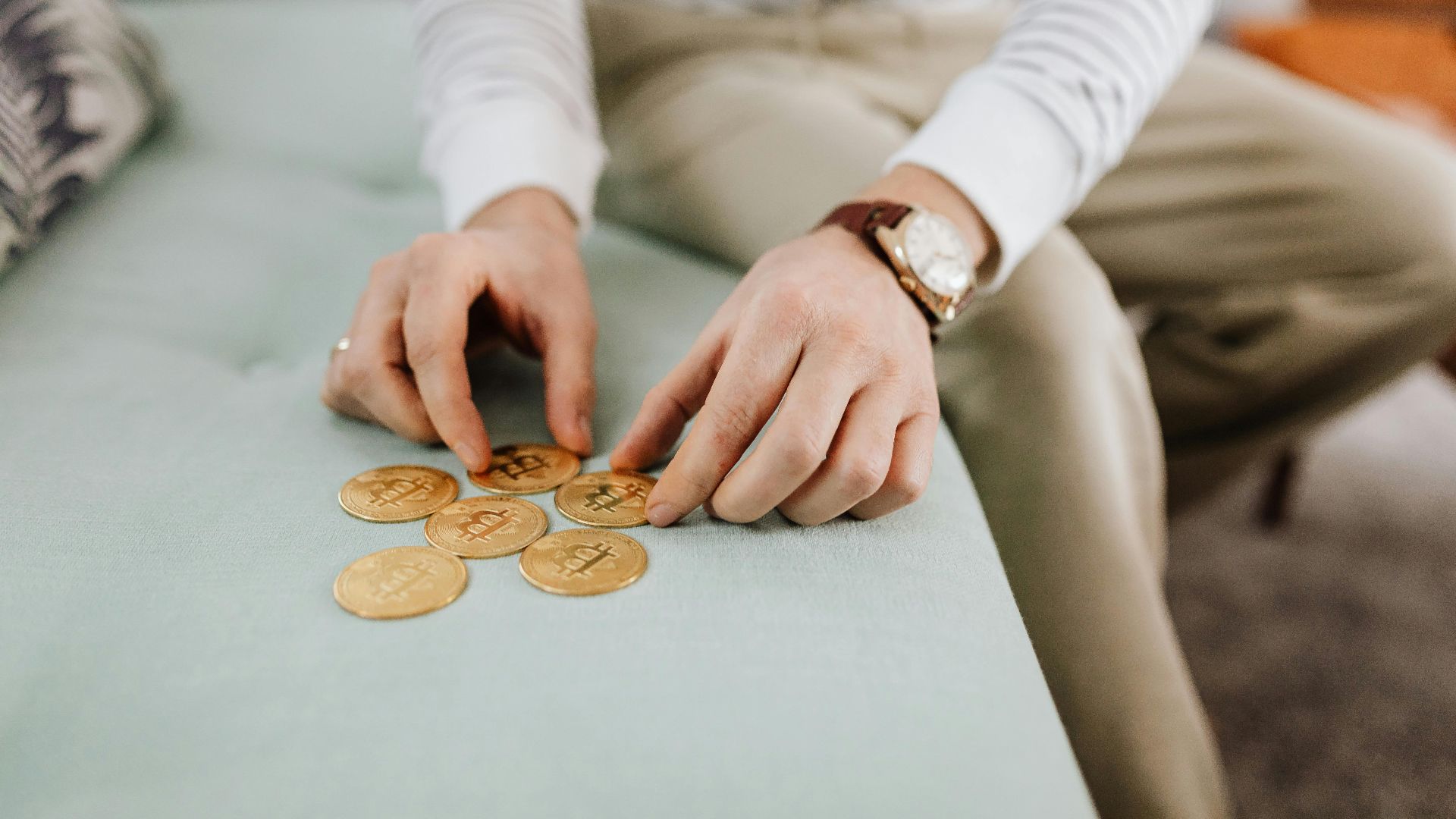 Close-up of hands organizing gold Bitcoin coins on a sofa, symbolizing digital currency management.