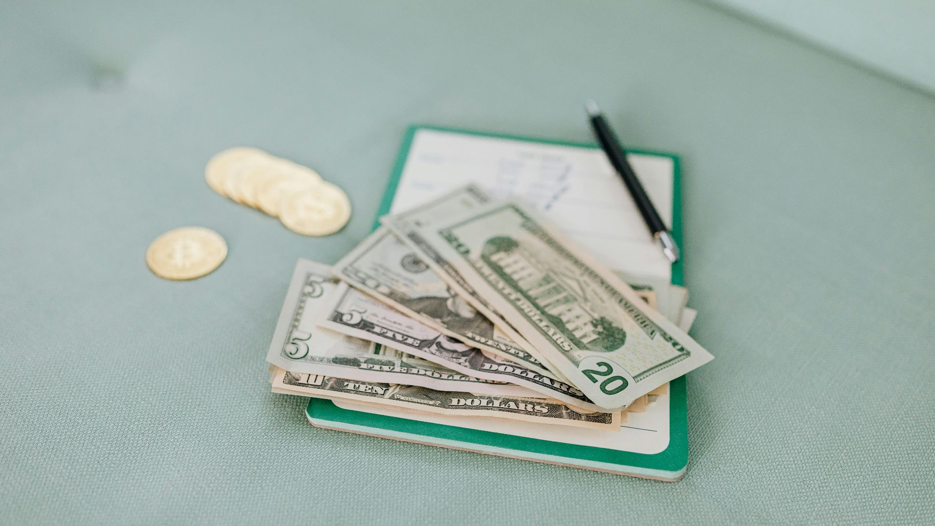 Close-up of American dollar bills and coins on a journal with a pen, representing budget planning.