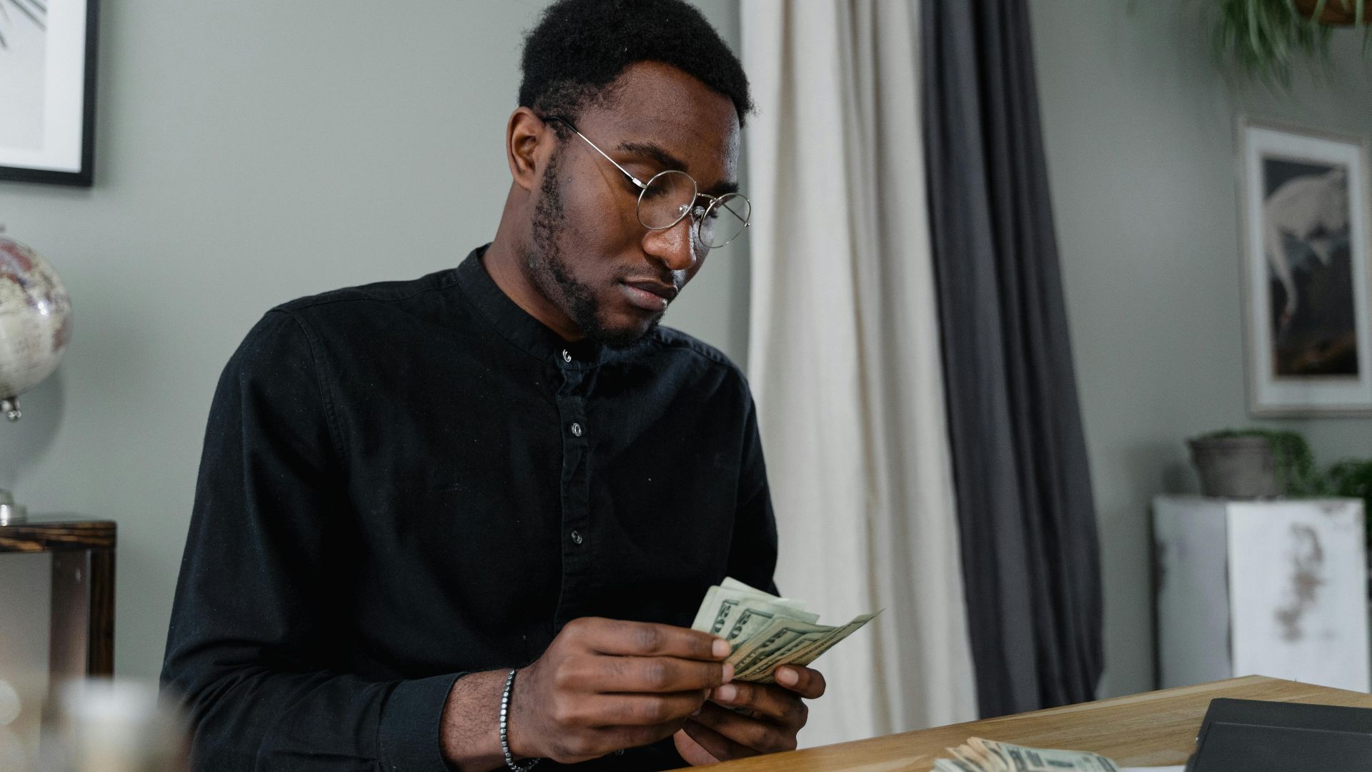 A focused man in glasses counting cash at a desk, indicating financial management.
