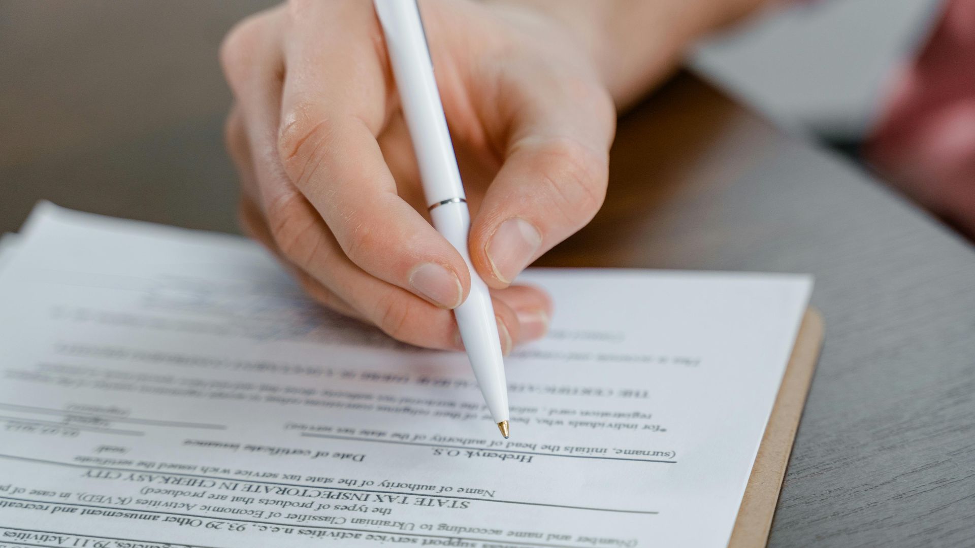A hand holding a pen signing a document, close-up shot with focus on the paper.