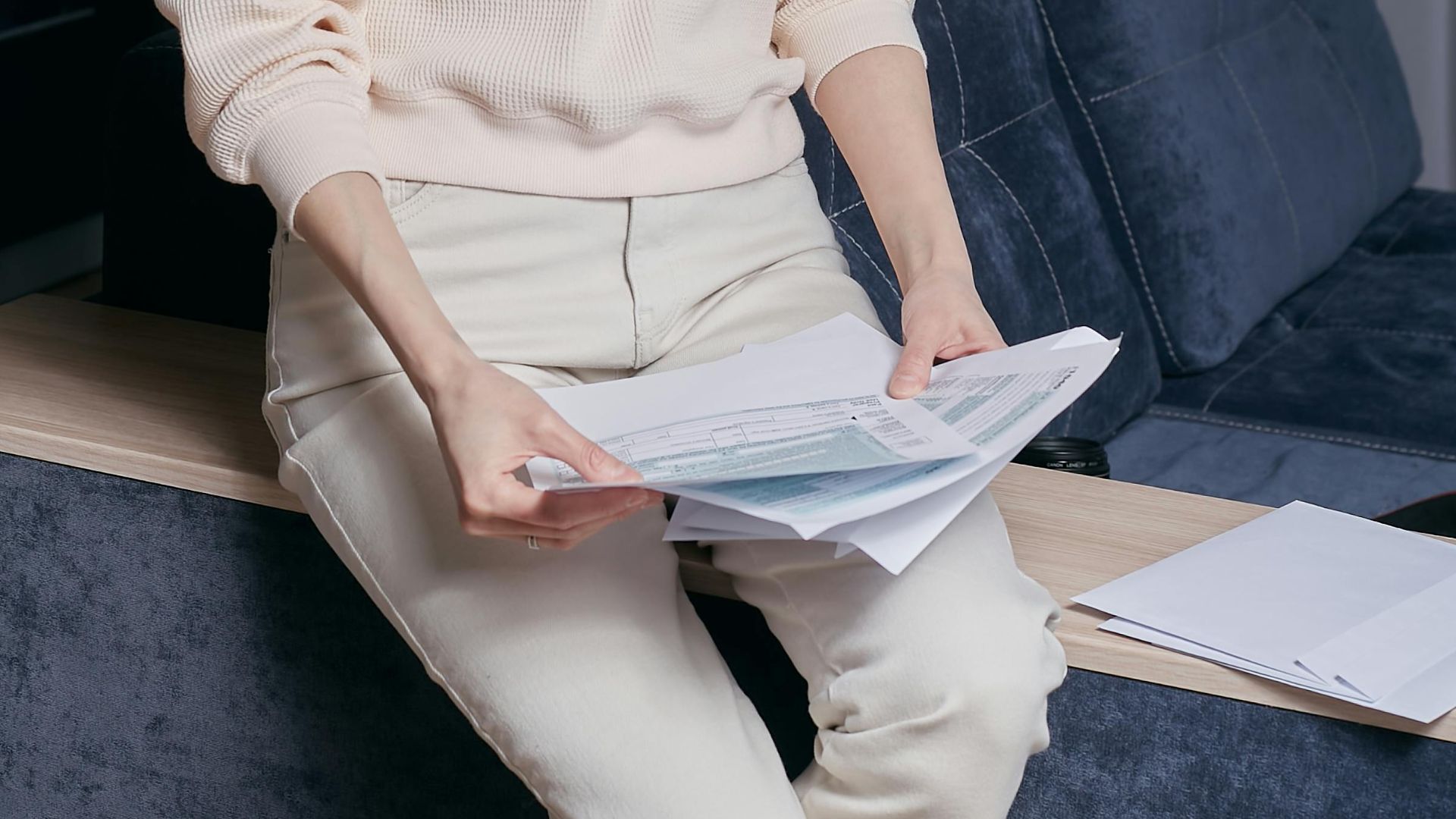 A woman sitting indoors reviewing documents in a comfortable and modern setting, wearing casual attire.