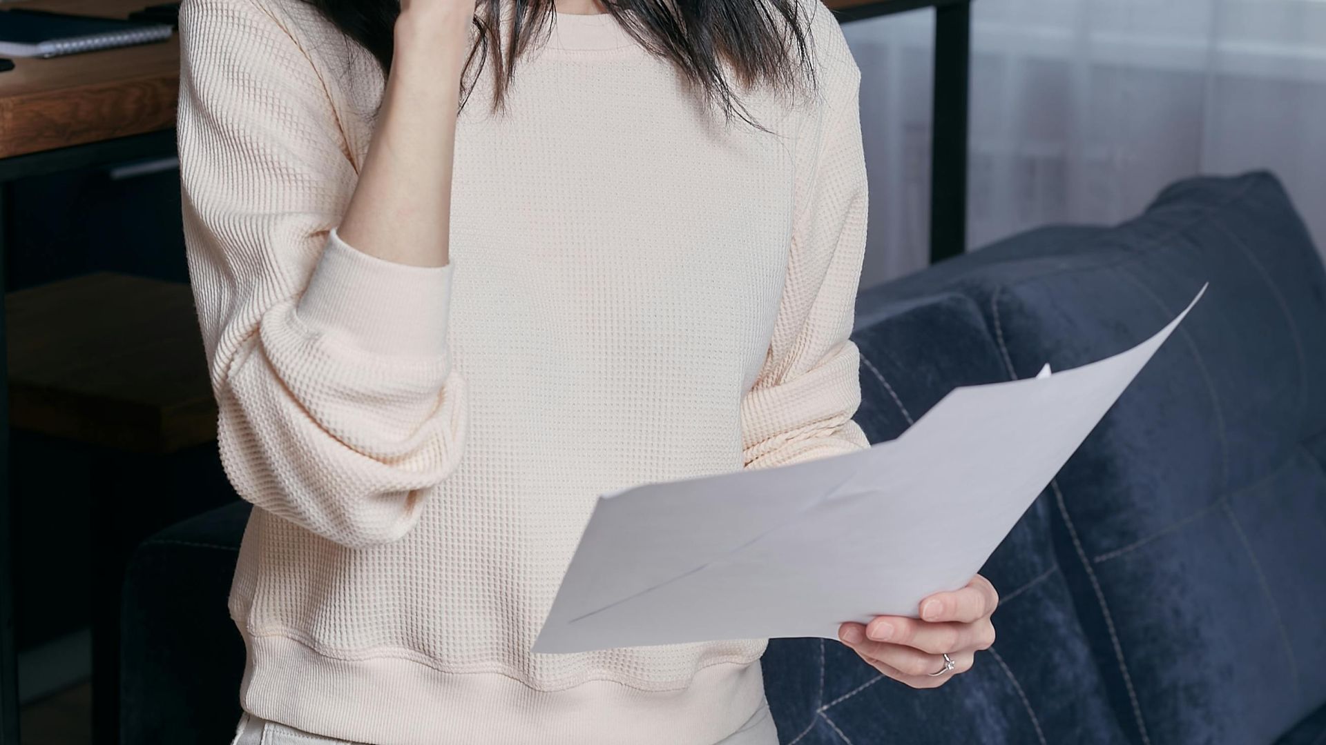 Young woman with eyeglasses assessing financial papers with a concerned look in a modern home setting.