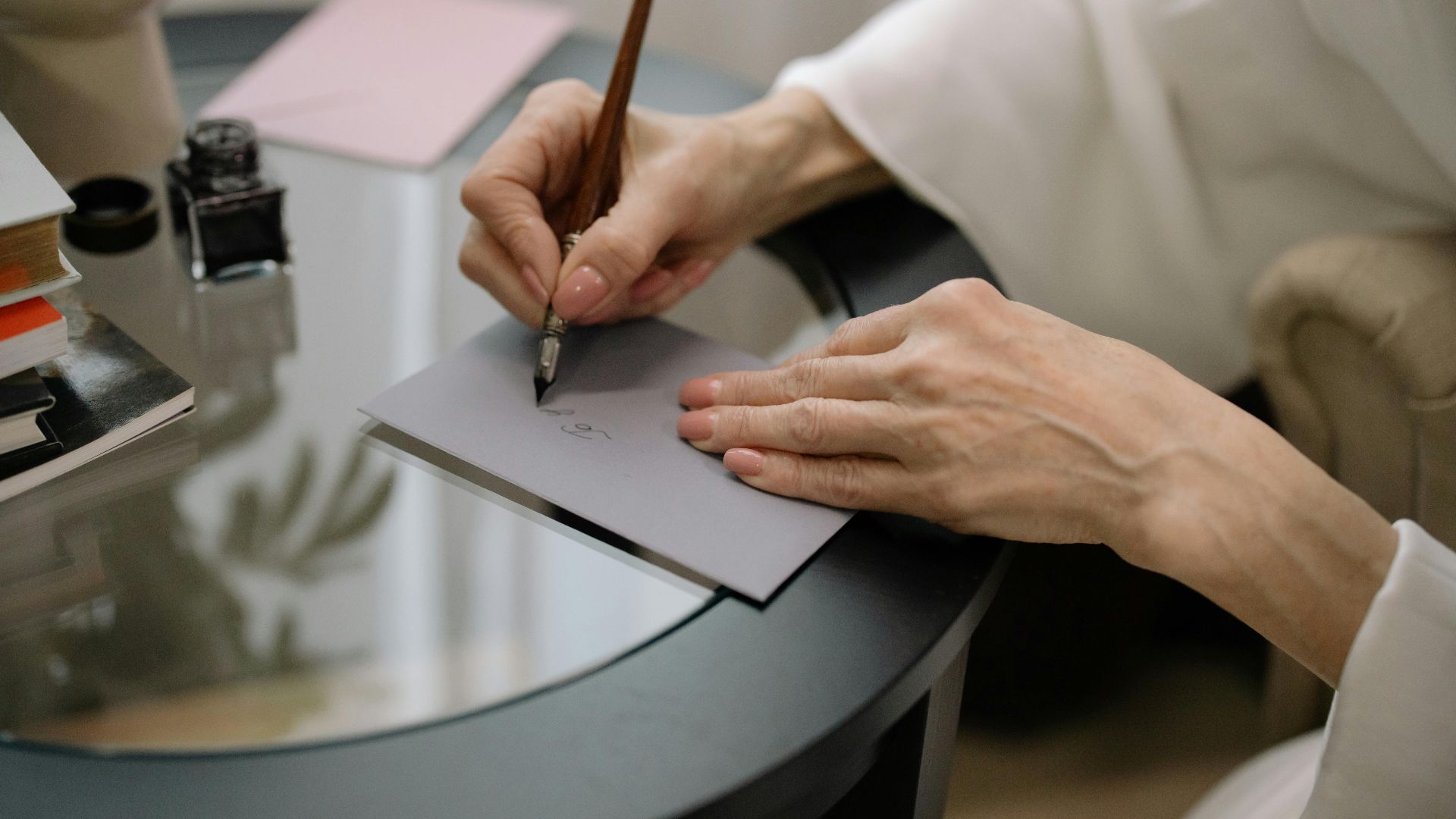 Close-up of hands elegantly writing on a gray envelope using a fountain pen.