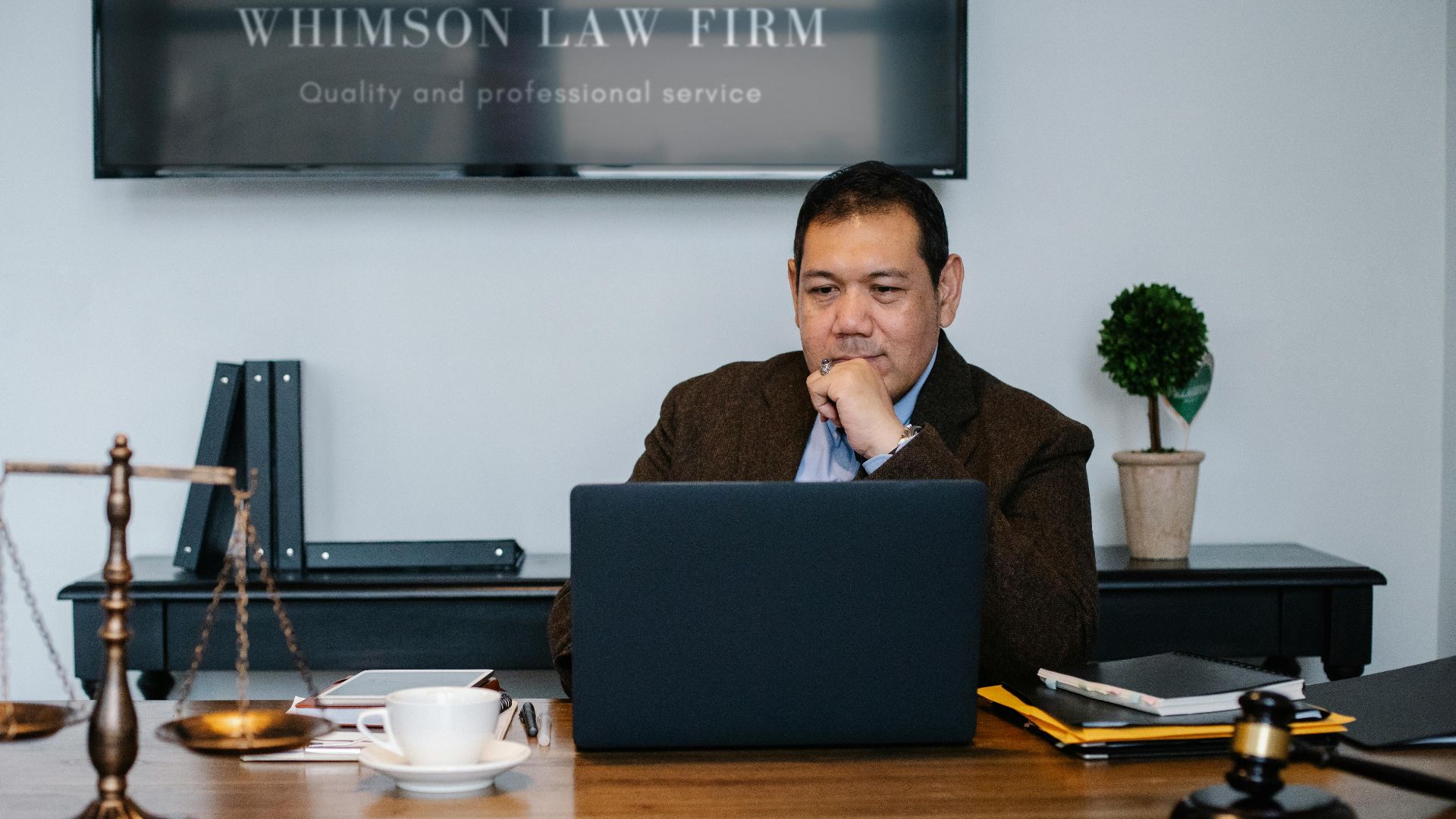 Serious ethnic mature man in formal outfit working with netbook at table with gavel