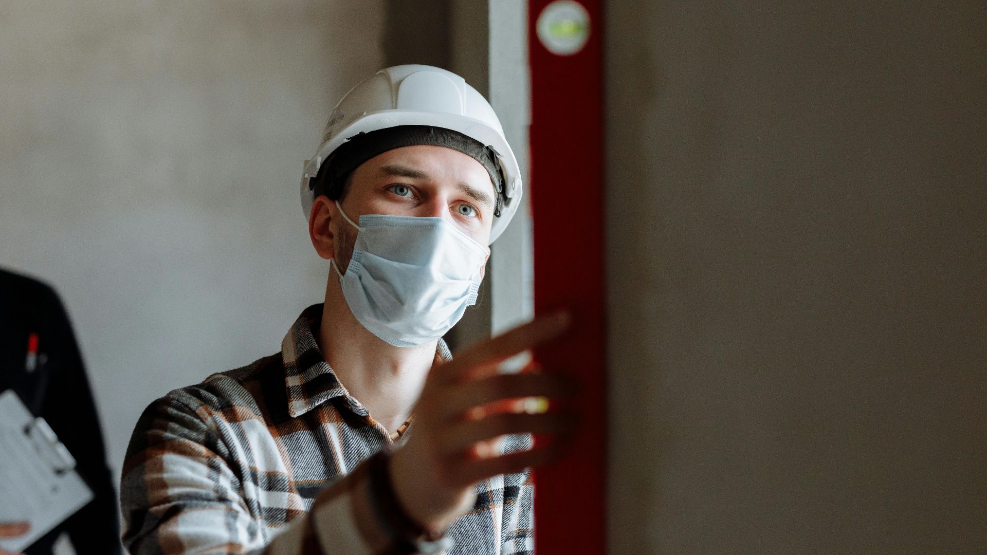 Man wearing a face mask and hard hat conducting safety inspection indoors.