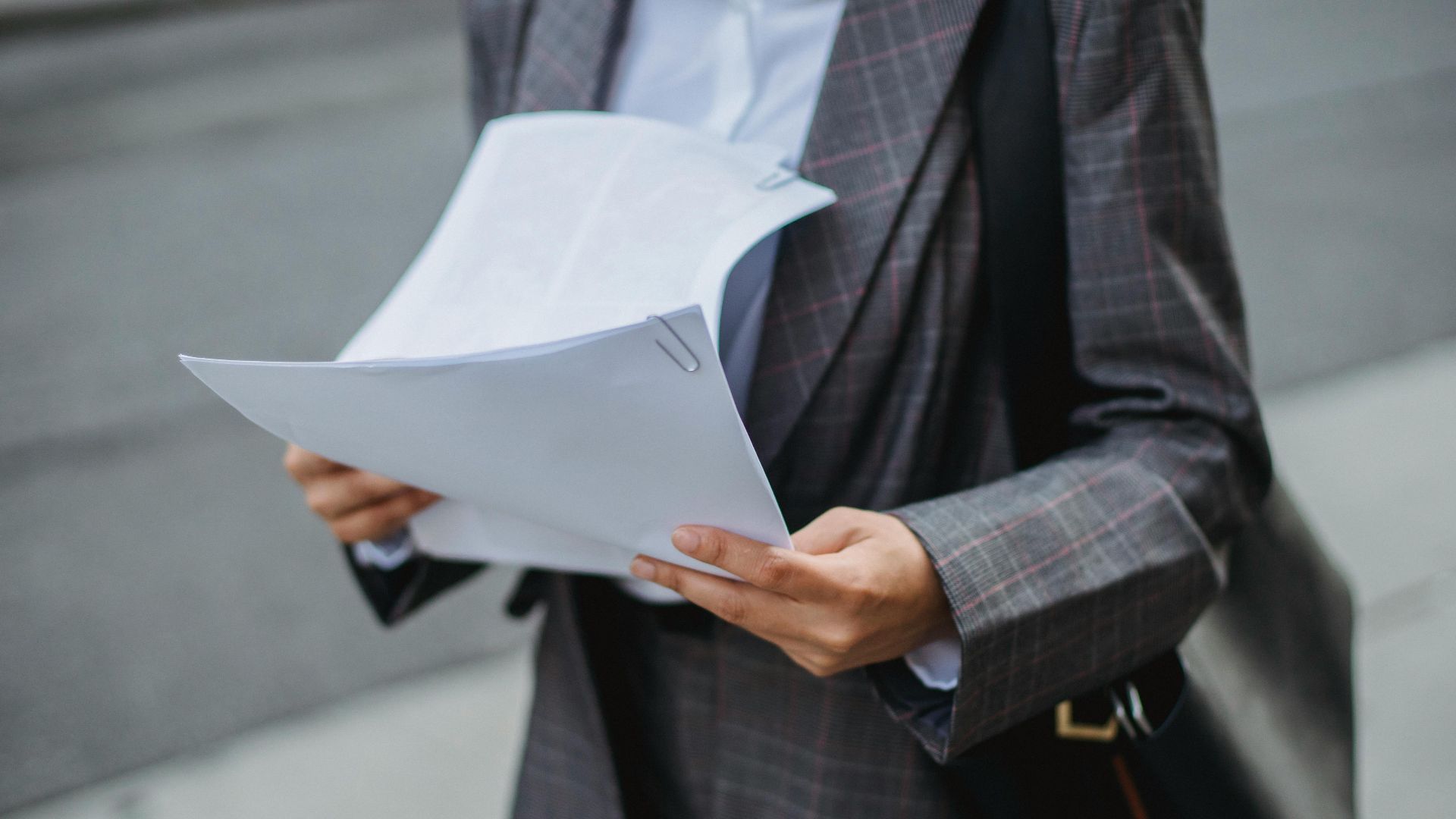 Professional businesswoman reviewing documents outdoors in a city environment.