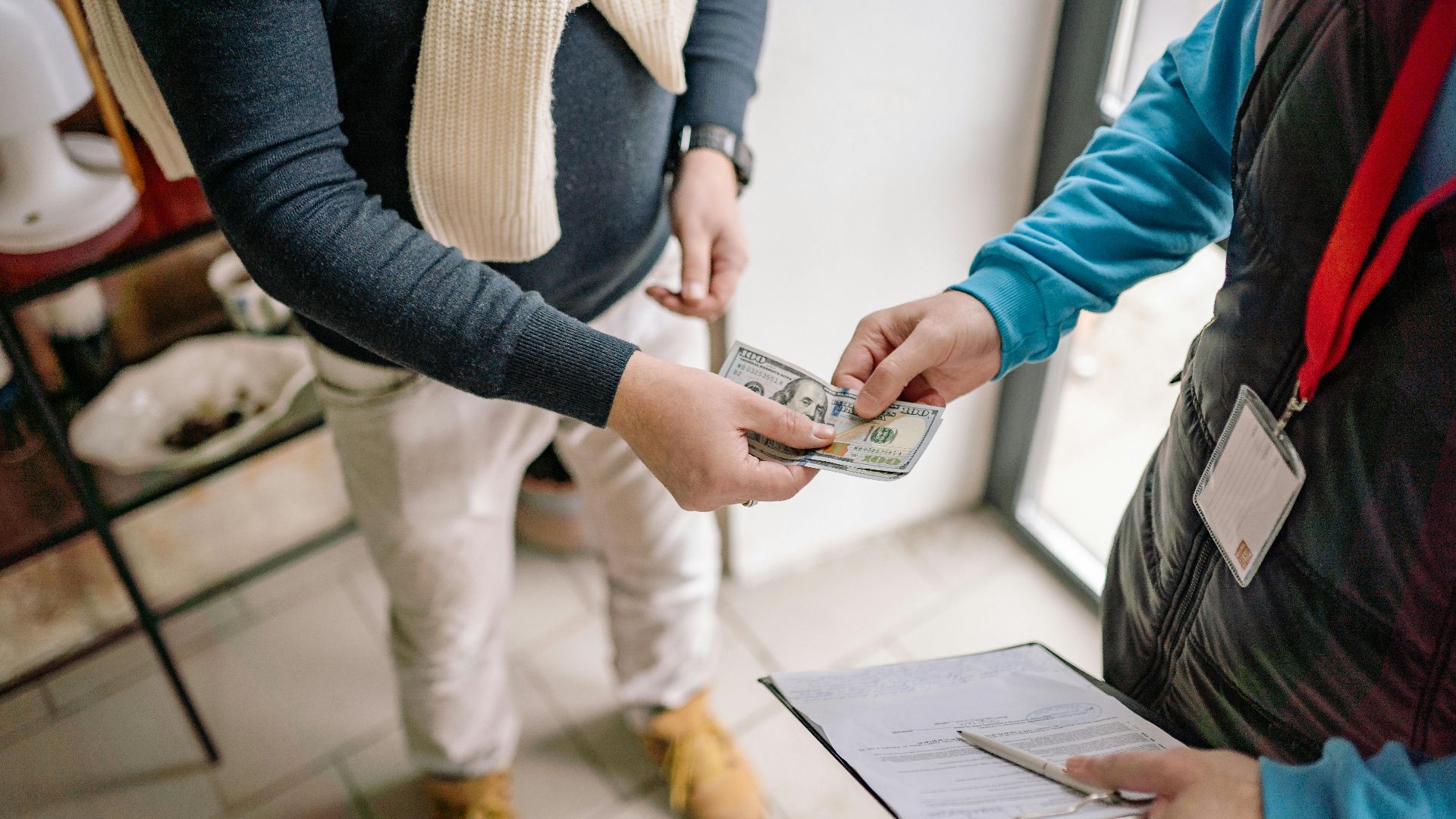 Close-up of hands exchanging cash during a transaction indoors, highlighting payment details.