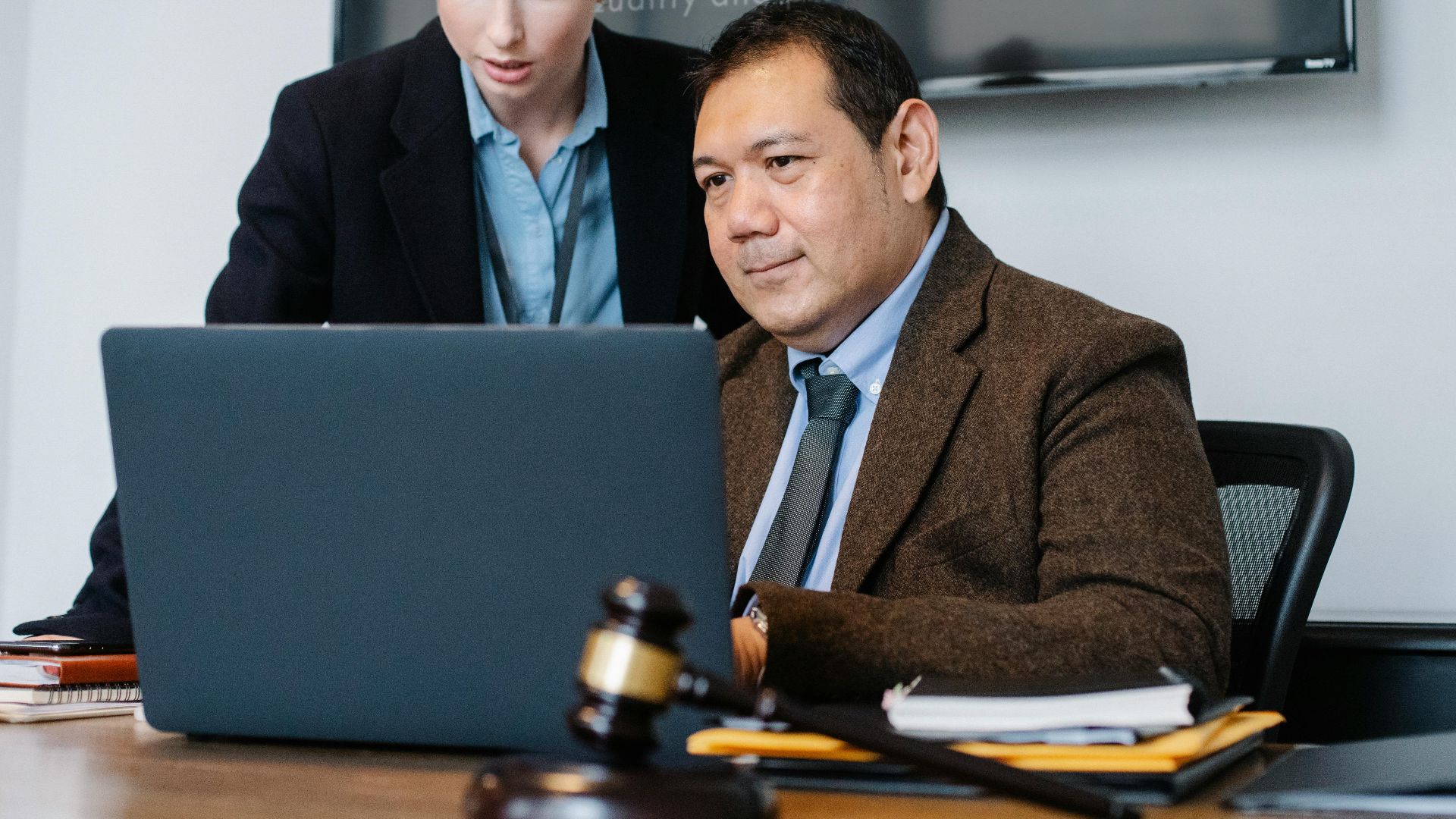 Smart mature ethnic judge in suit working on laptop and discussing details of new case with young female assistant in law firm