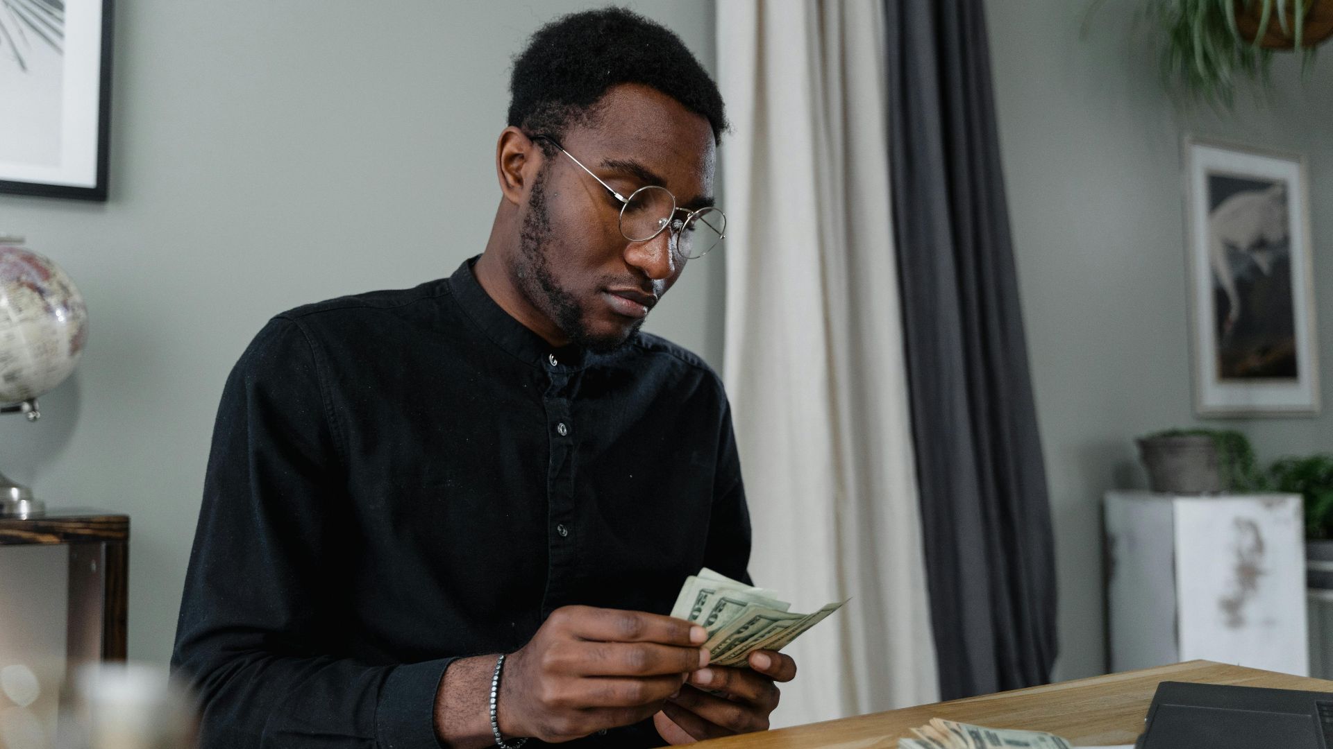 A focused man in glasses counting cash at a desk, indicating financial management.