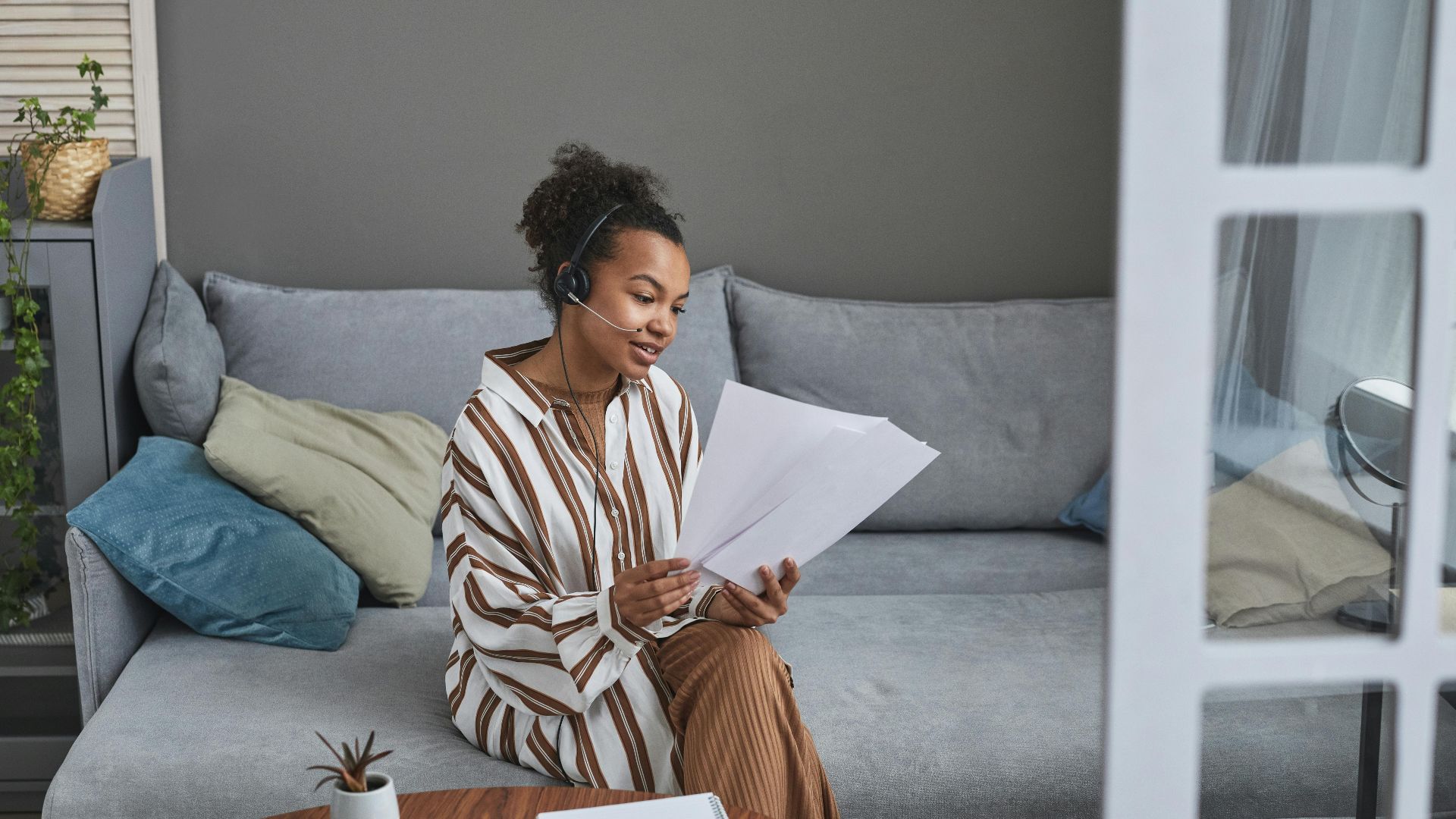 Woman in a home office setting working remotely with headset and documents.