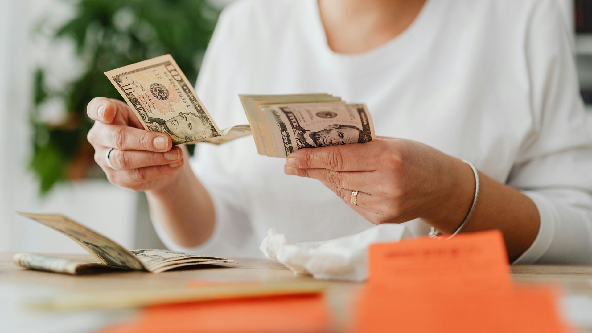 A woman sits indoors counting cash at her office desk, focusing on finances.