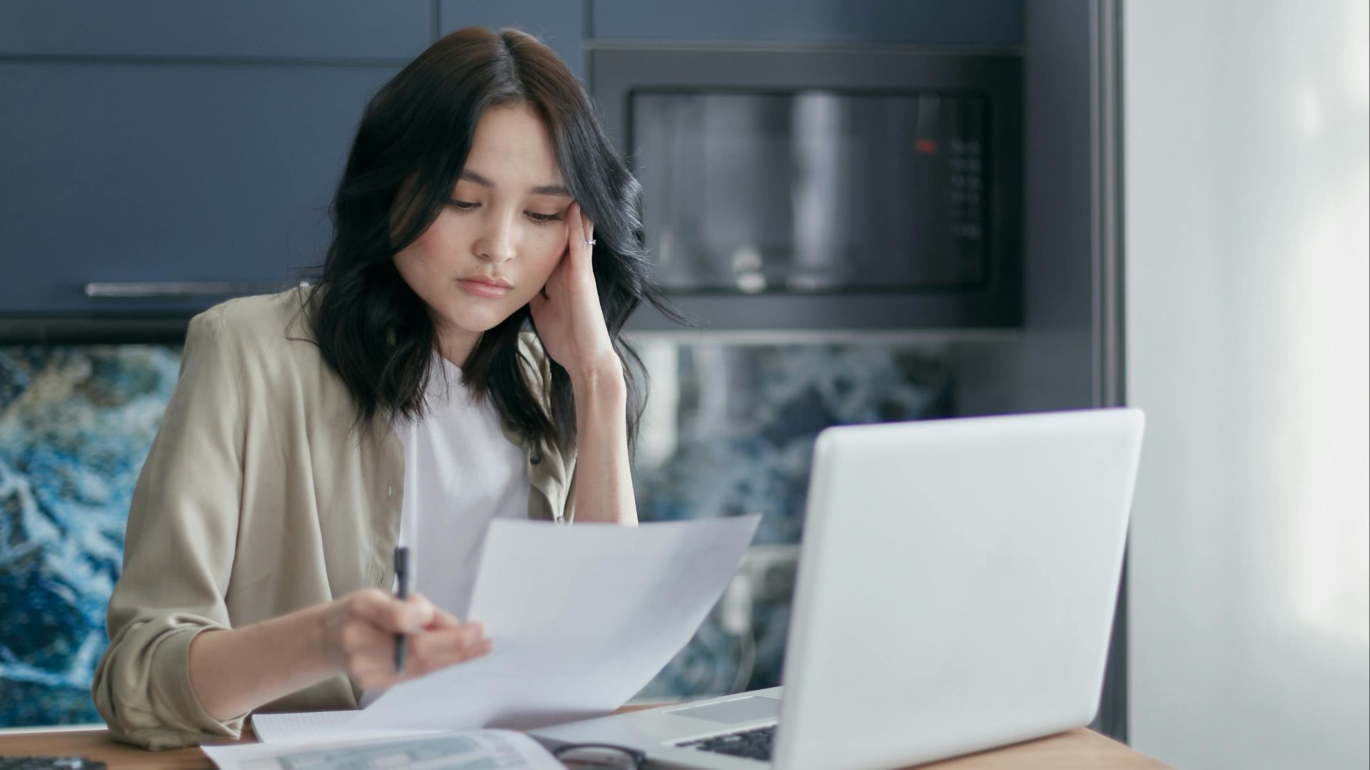 Focused young woman reviewing financial documents with a laptop in a home office setting.