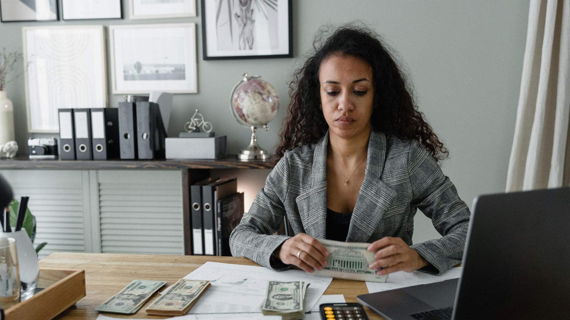 Focused woman counts cash at desk surrounded by office items, emphasizing finance and professionalism.