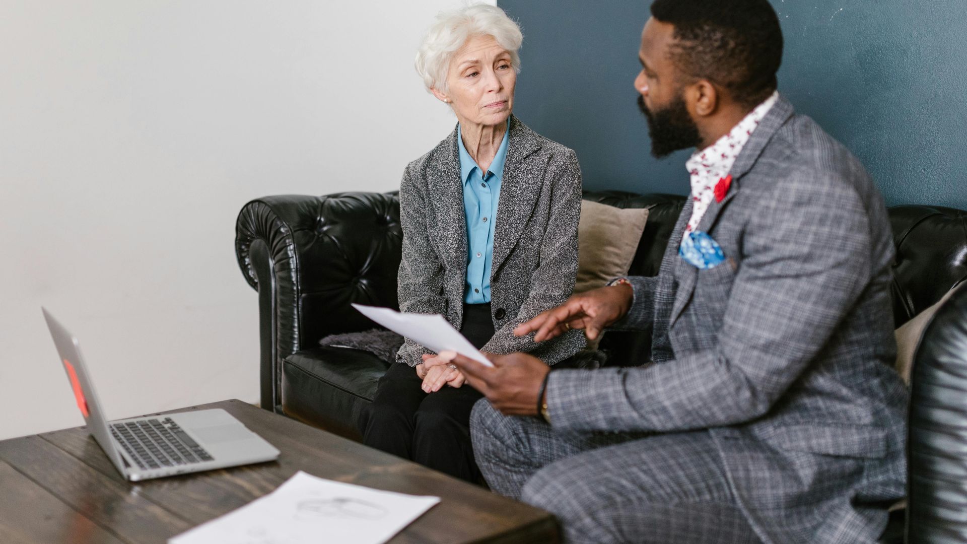 An elderly woman and a man in a professional meeting discussing documents indoors.
