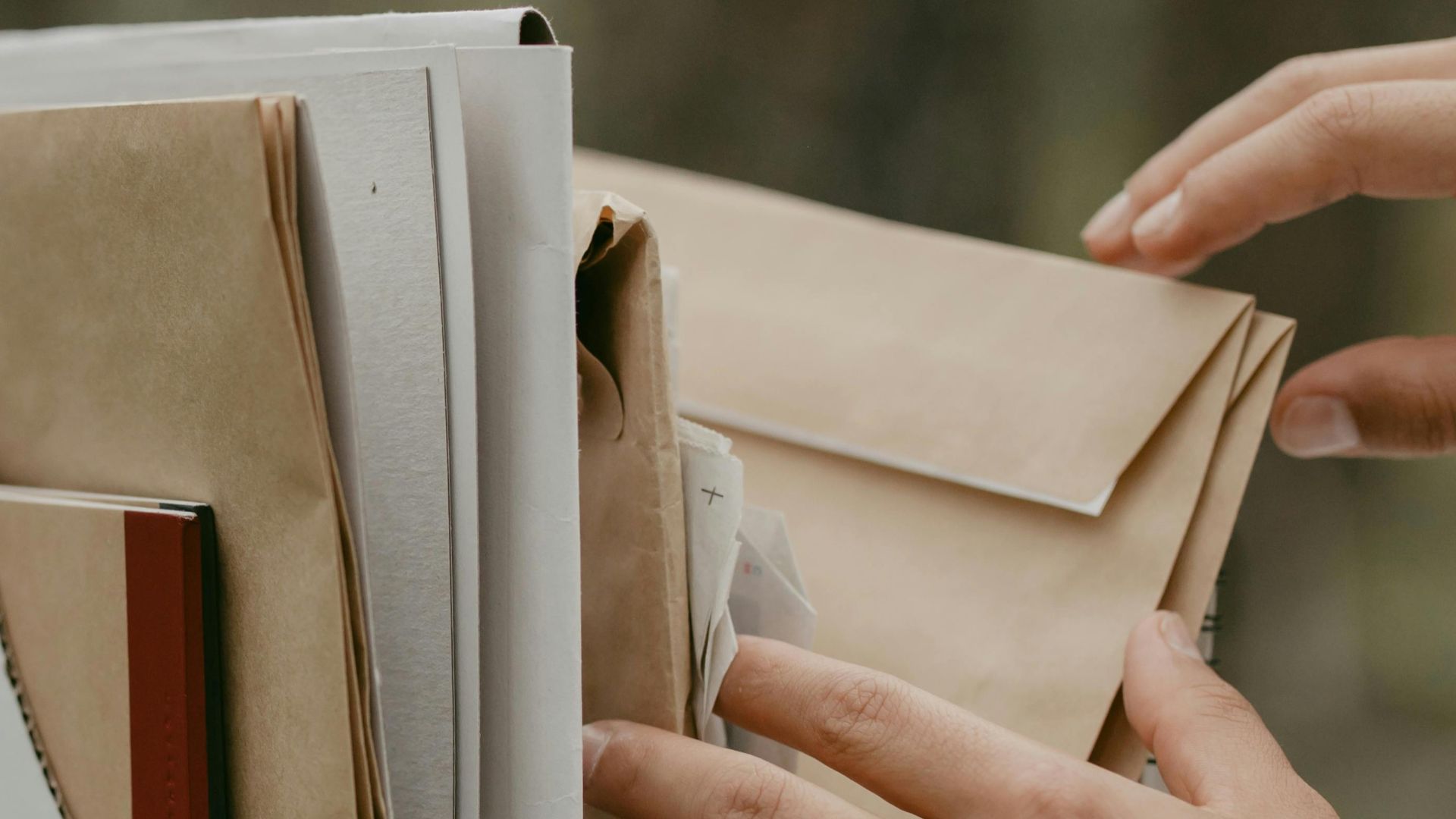 Close-up of hands sorting and organizing documents in a file box outdoors.