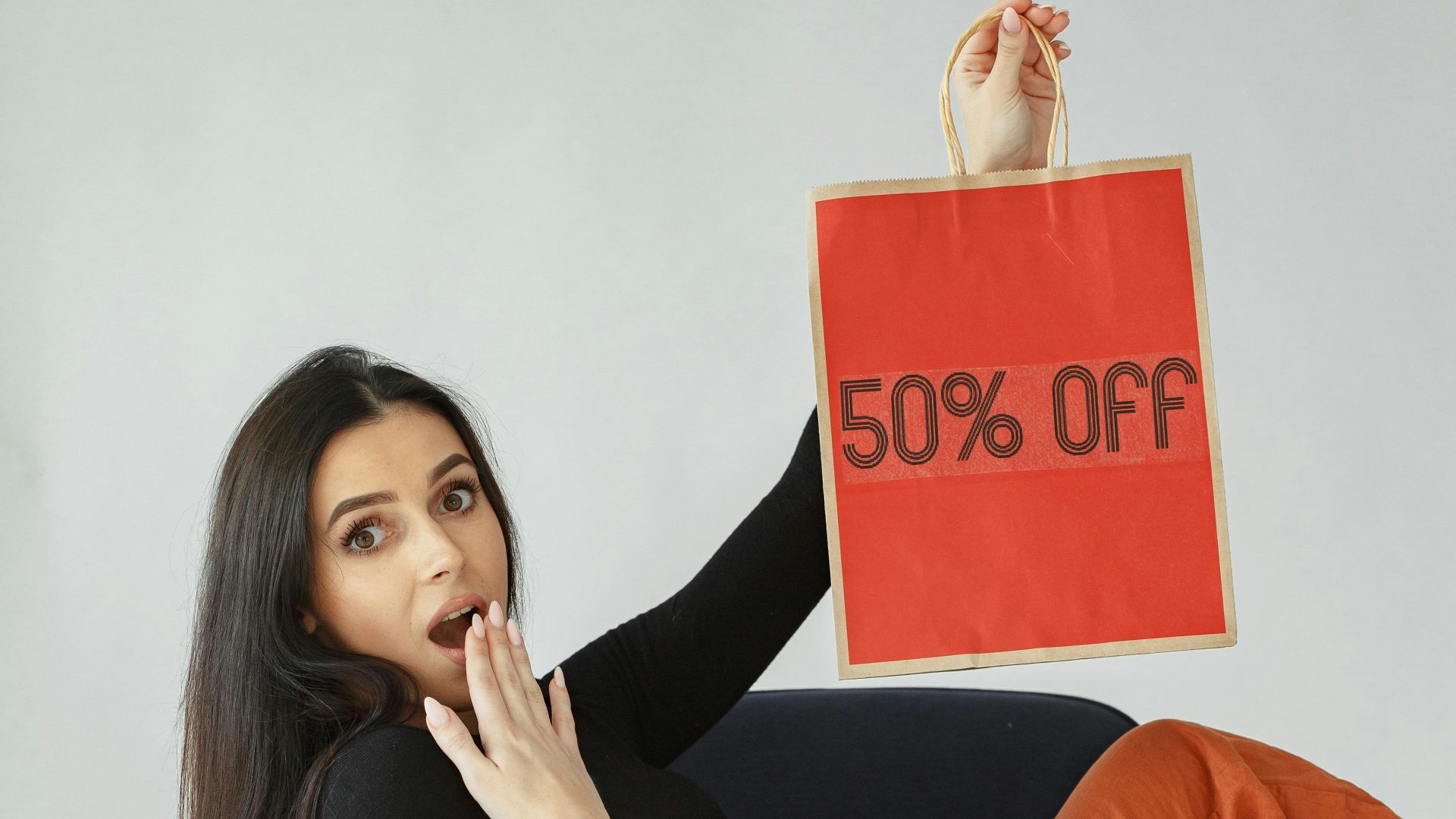 Stylish young woman sitting with shopping bags, showcasing a '50% Off' sale sign.
