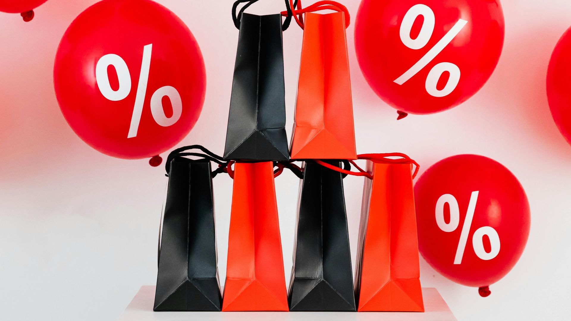 Vibrant red balloons with percentage signs and shopping bags for sales event.
