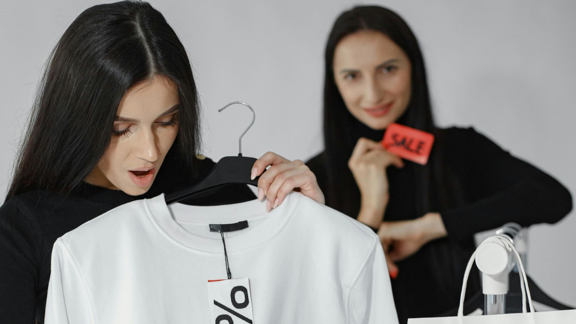Woman holding a discount-tagged white shirt during Black Friday sale indoors.