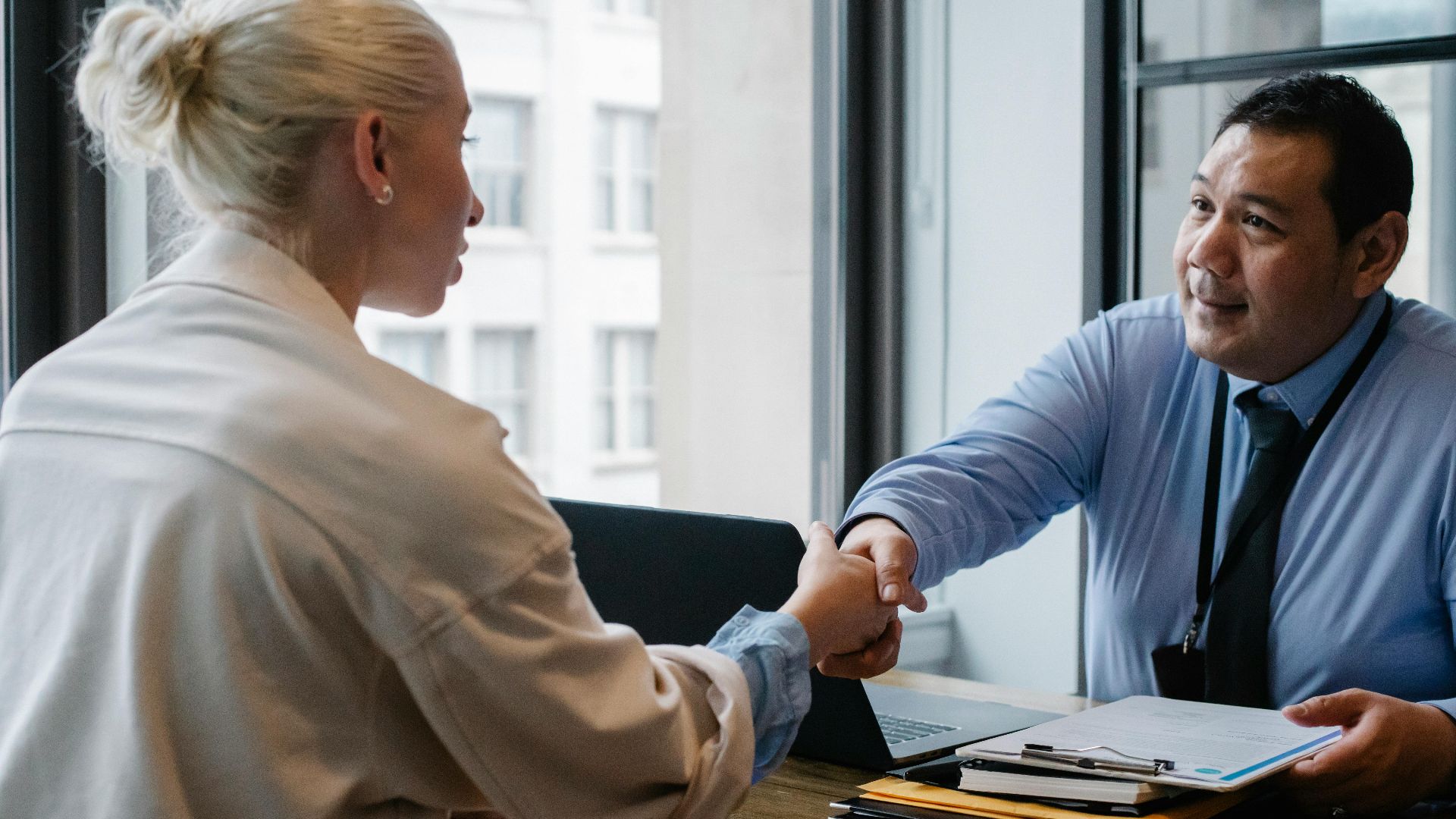 Two professionals in an office setting shaking hands after a business agreement.