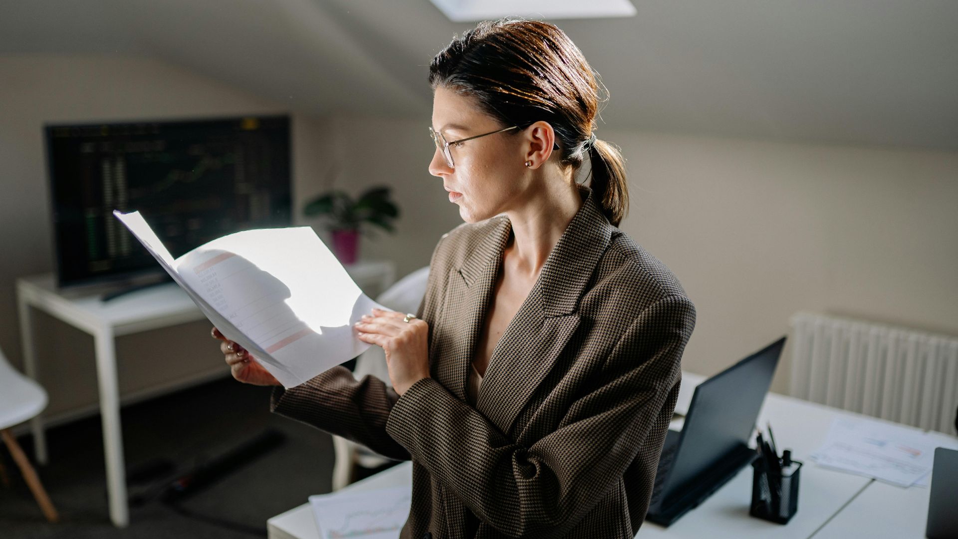 Professional woman in glasses reviewing financial documents at her office desk.