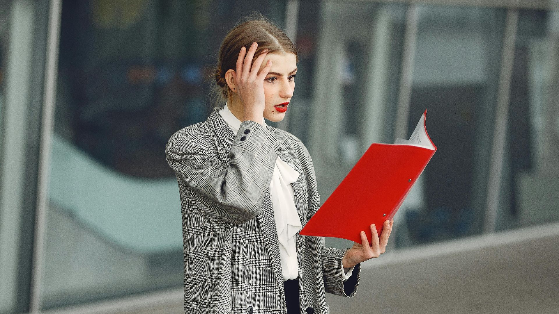 Woman in business attire looking stressed while holding and reading documents outside.