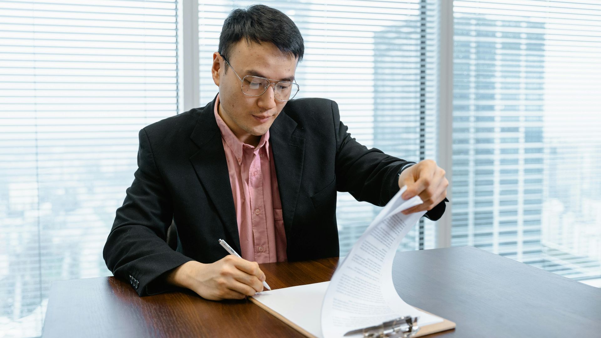 Asian businessman in formal wear signs paperwork at office desk.