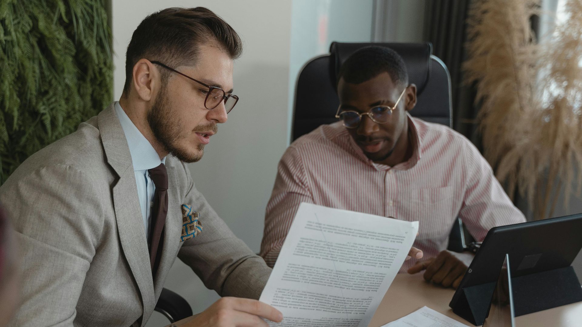 Two businessmen in an office discussing documents and working together.