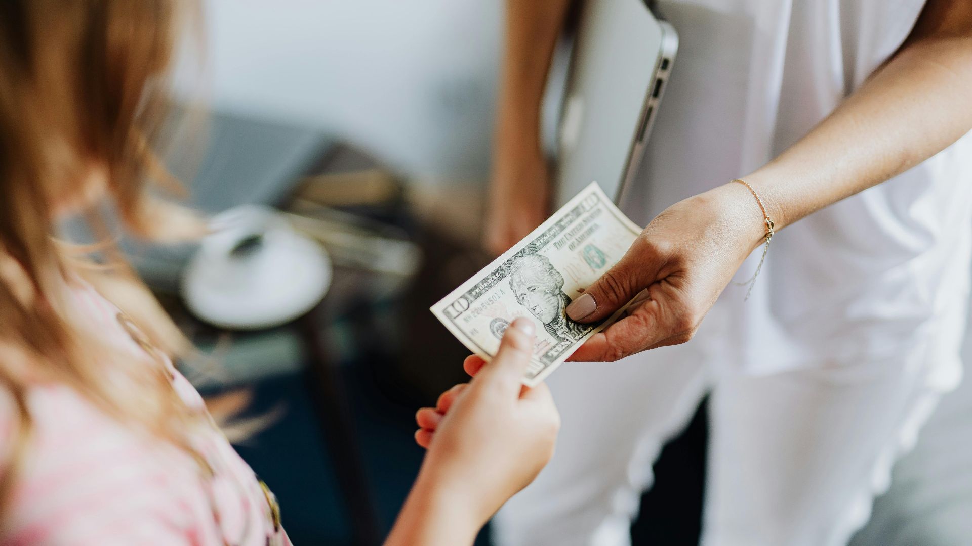 Close-up of a transaction involving a US dollar bill exchanged indoors between two individuals.