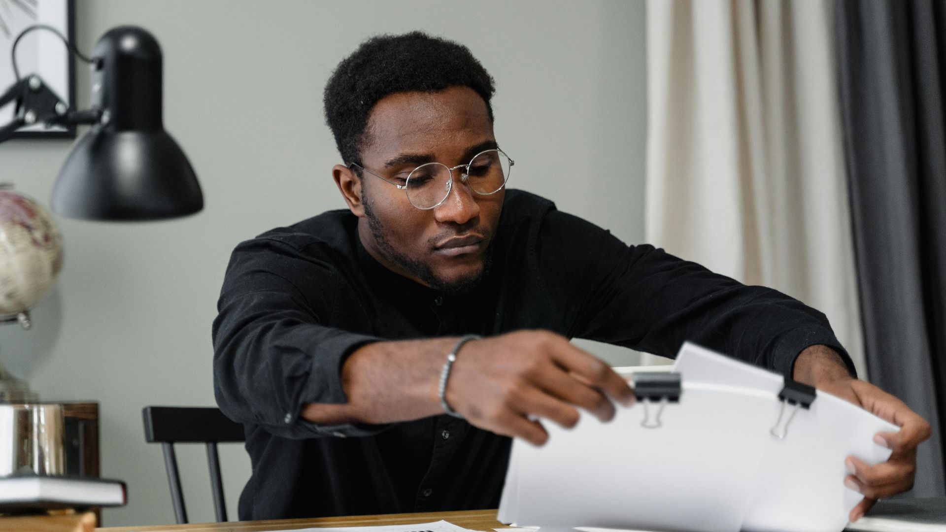 Professional man with glasses reviews documents at a desk in an office setting, emphasizing concentration.