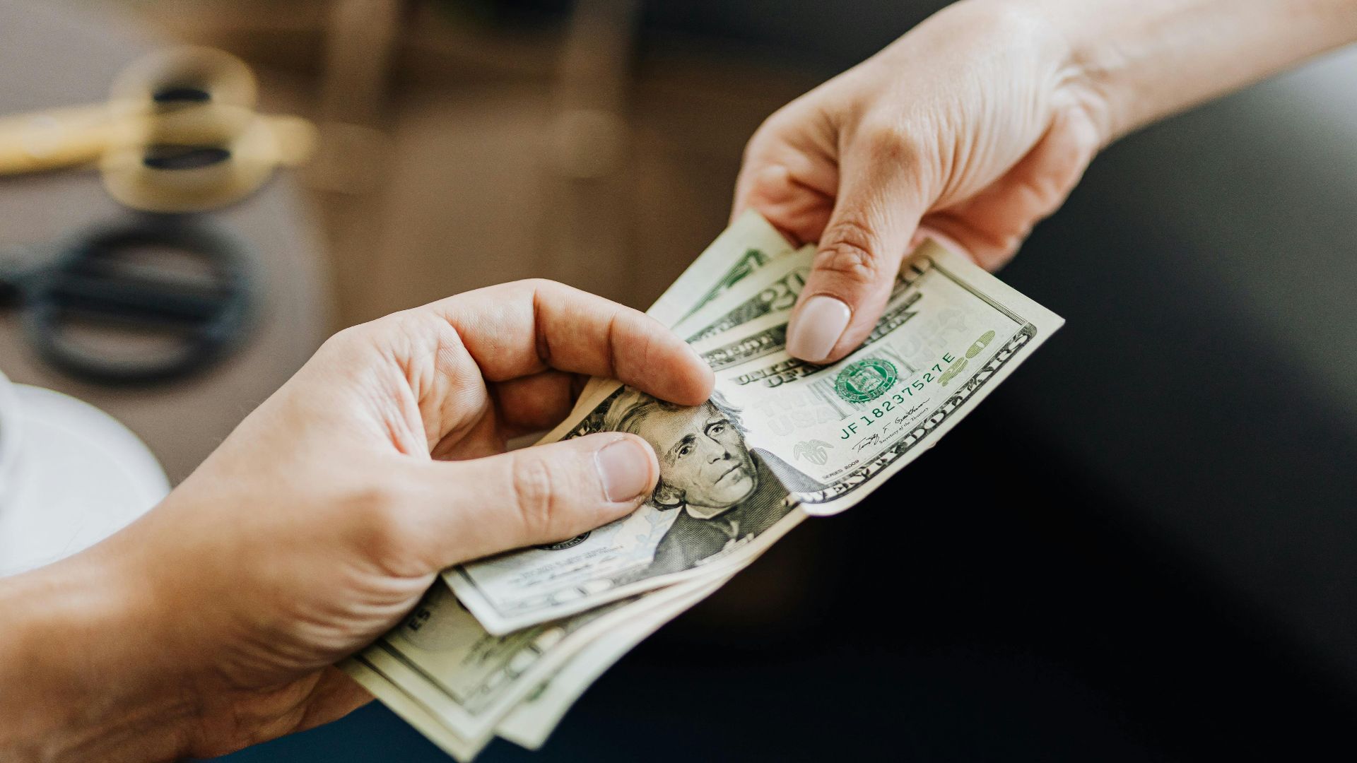 A close-up image of hands exchanging US dollar bills, symbolizing financial transaction or payment.