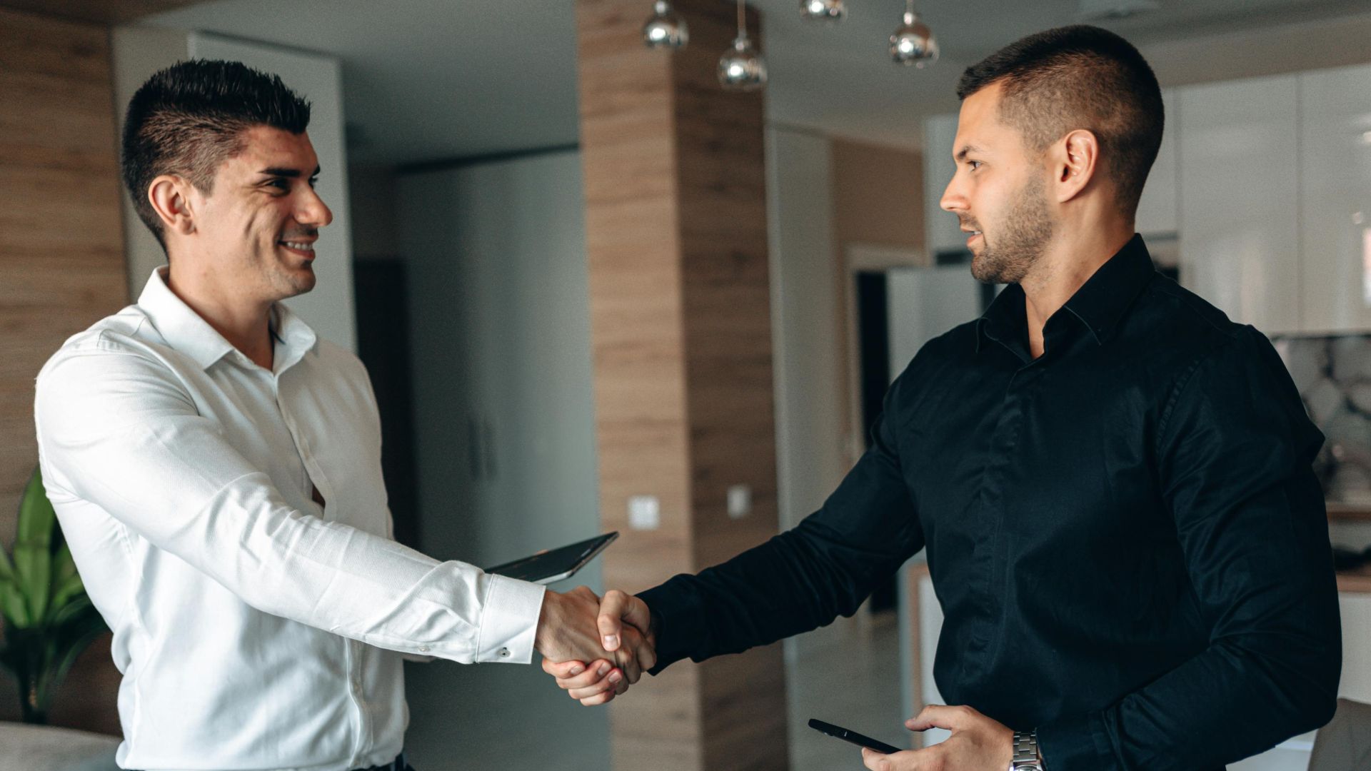 Two business professionals shaking hands in a modern office environment, symbolizing partnership.