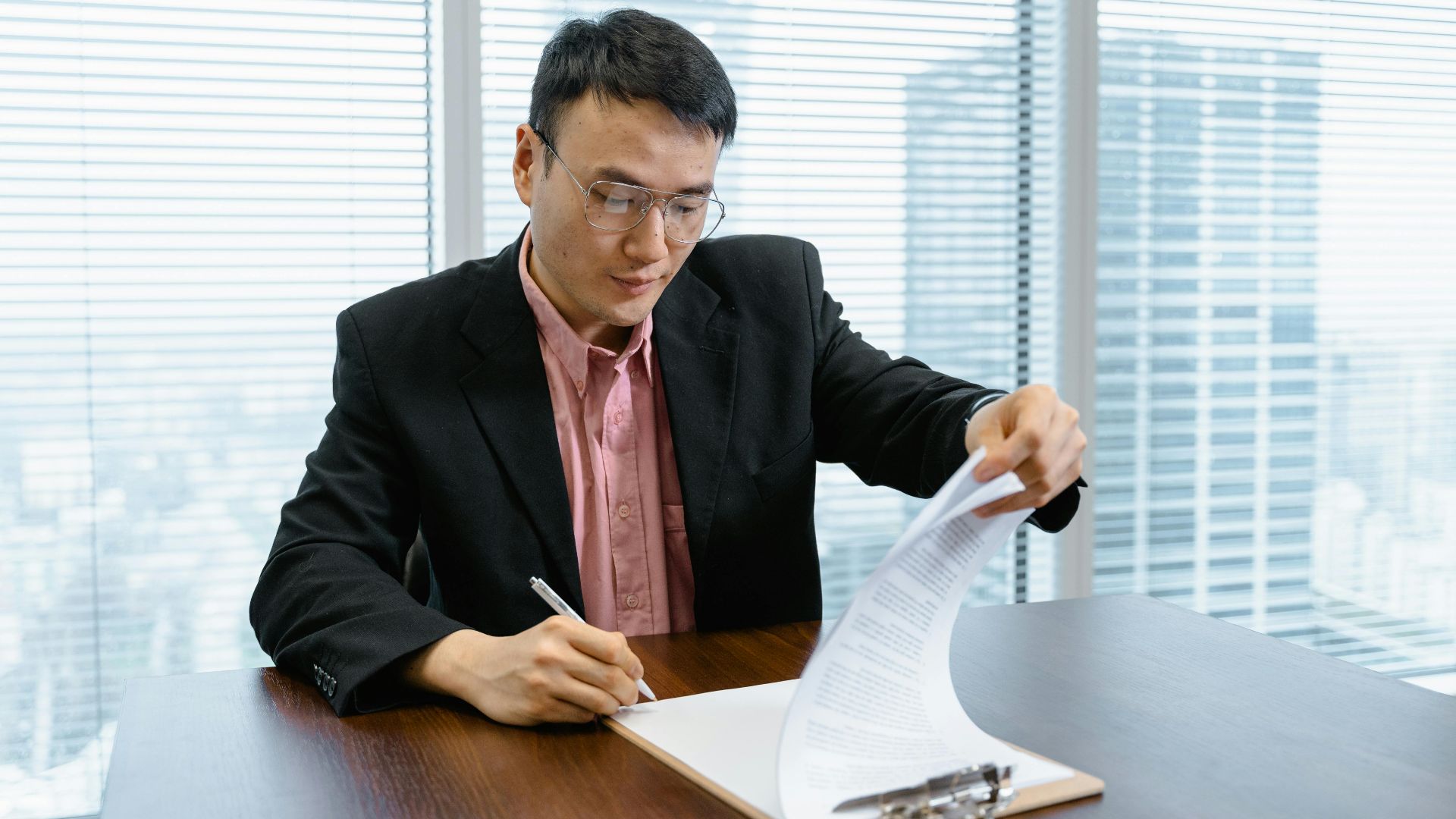 Asian businessman in formal wear signs paperwork at office desk.