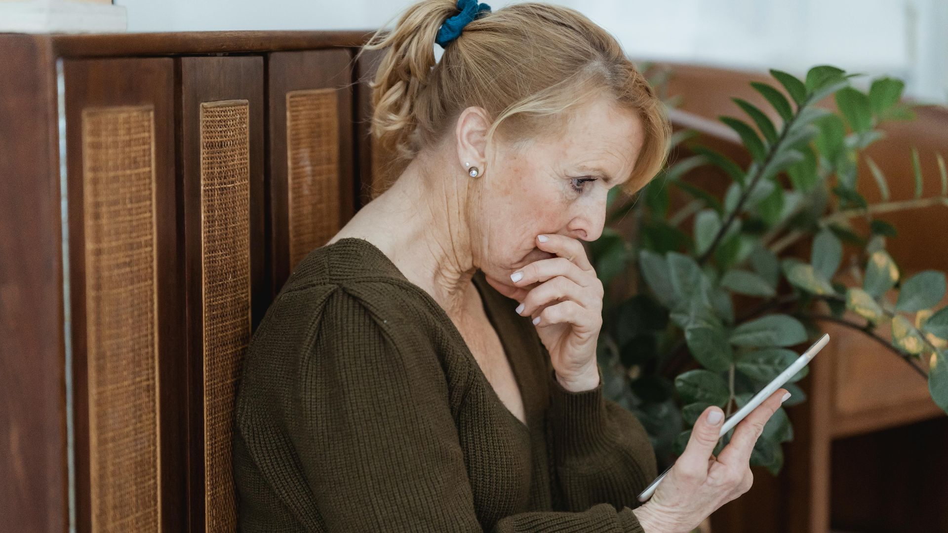 Senior woman deeply focused on her smartphone, indoors with plants and cozy decor.
