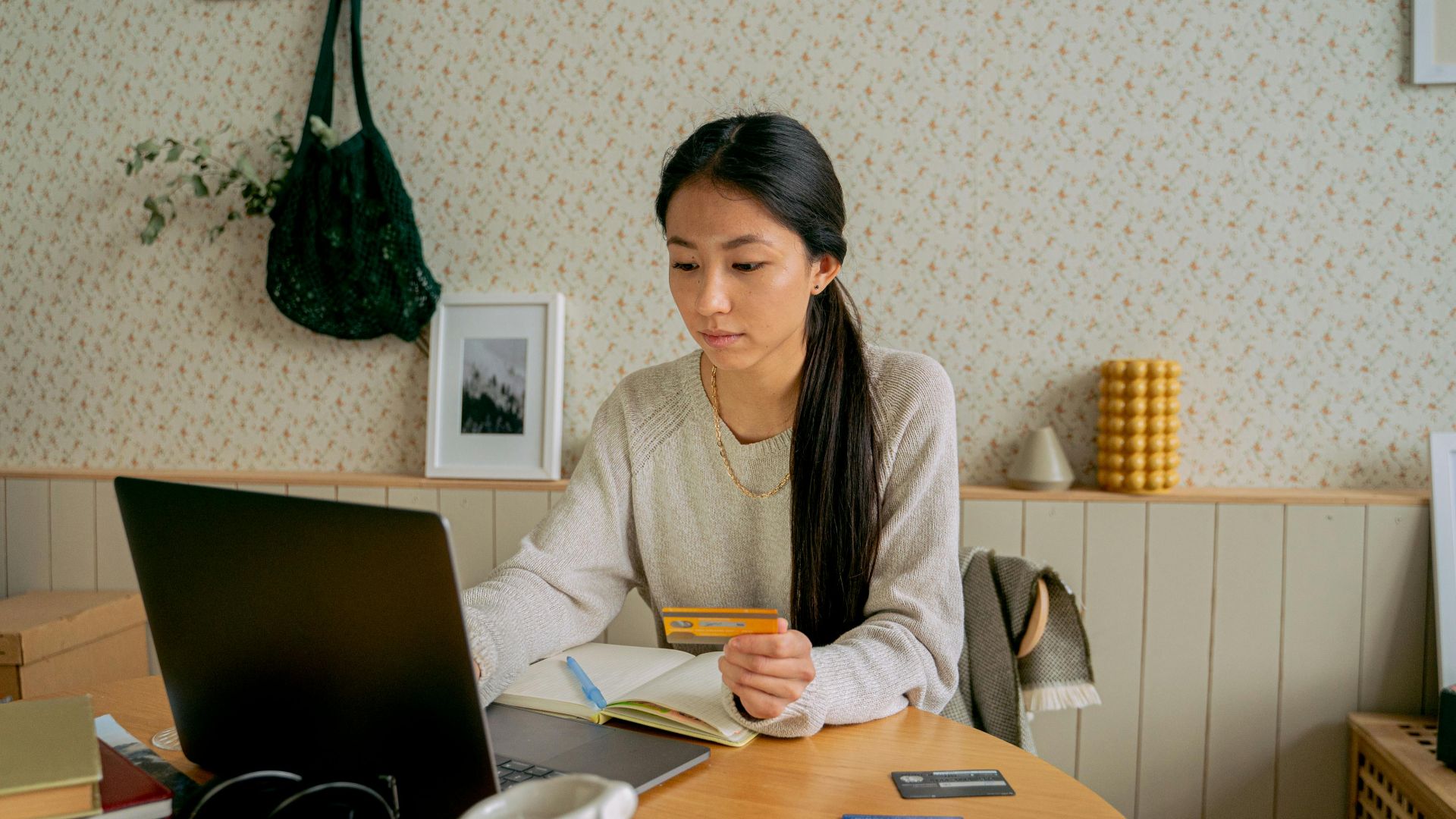 A woman using a laptop and credit card for online shopping at a cozy indoor setting.