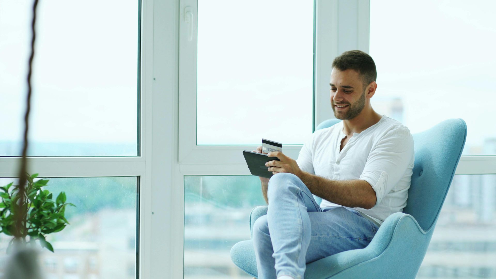 Smiling man shopping online using a tablet and credit card at home.