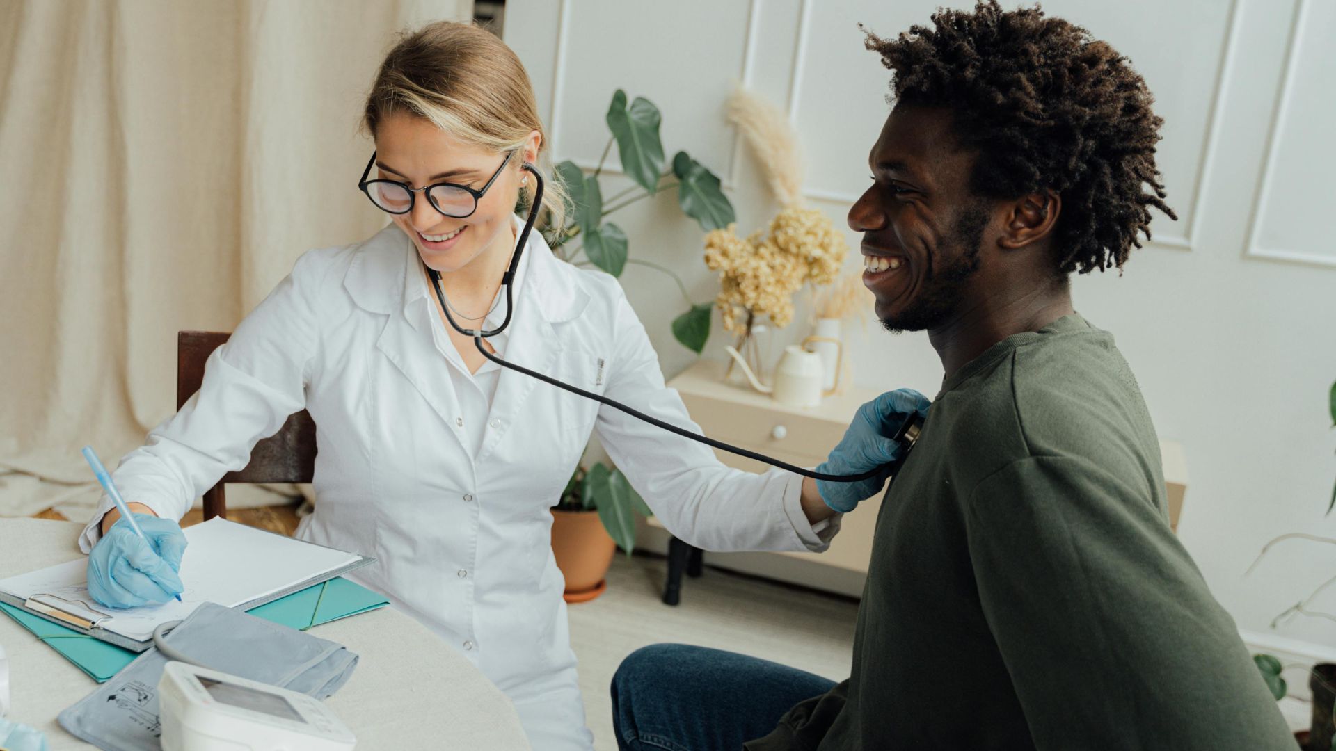 Caucasian female doctor checks black male patient's heart rate with stethoscope in a clinic.