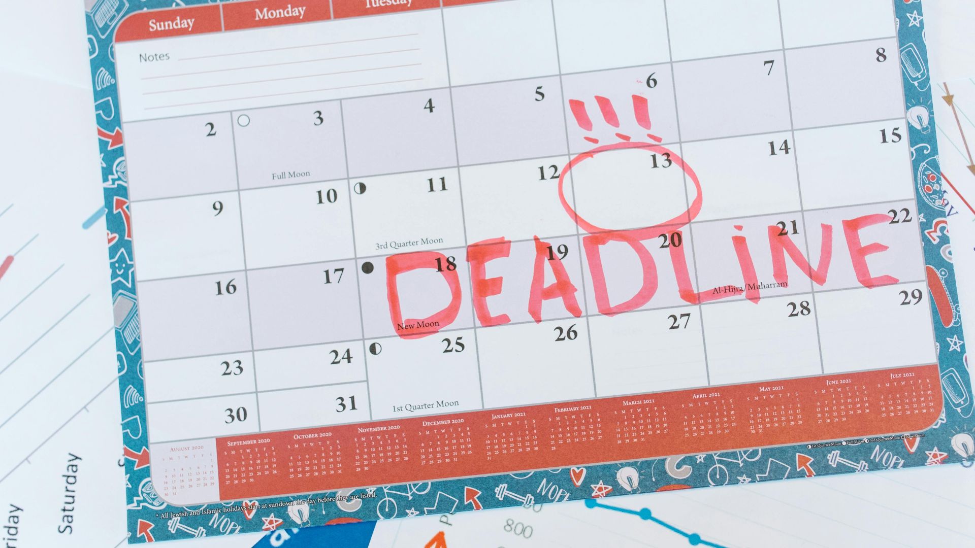 Vibrant August calendar on a desk with deadline marked in red, surrounded by graphs and charts.