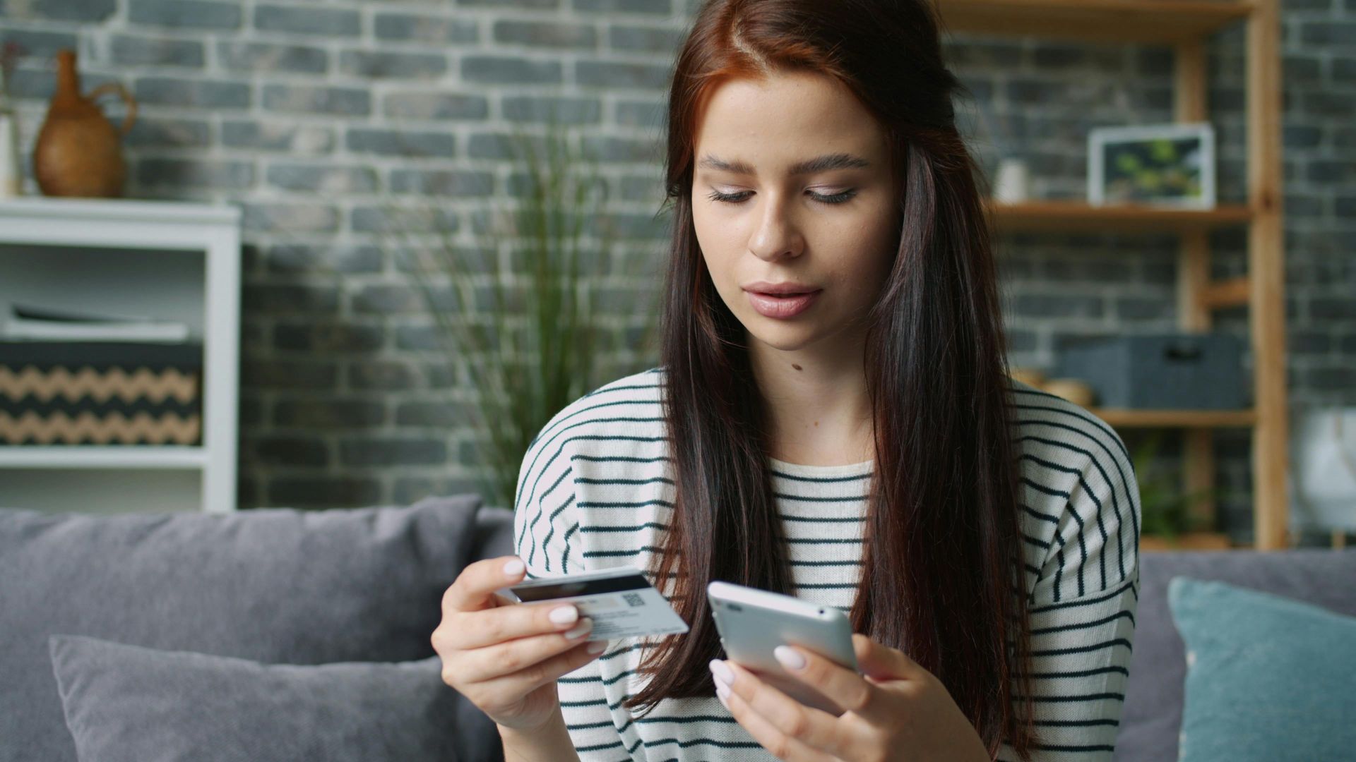 Woman using smartphone and credit card for online shopping in living room.