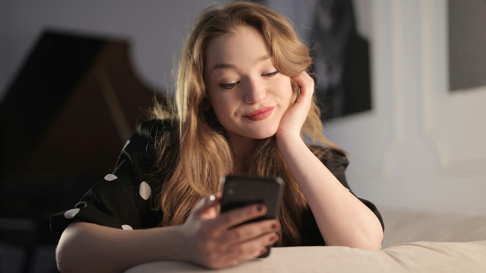 Smiling young woman enjoying leisure time on her smartphone in a cozy living room.