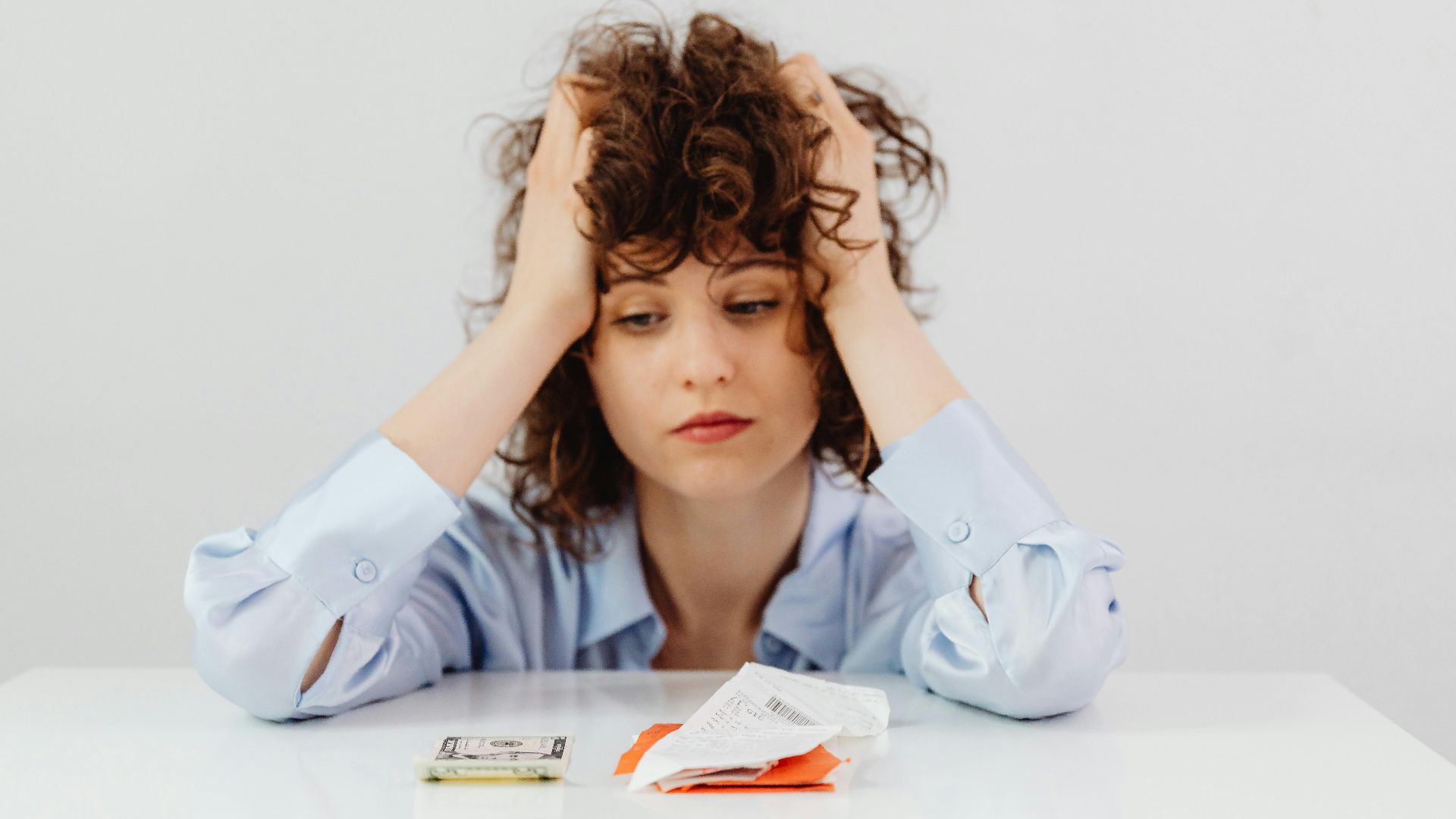 Woman in blue sleeves appears stressed while looking at receipts and money, symbolizing financial stress.