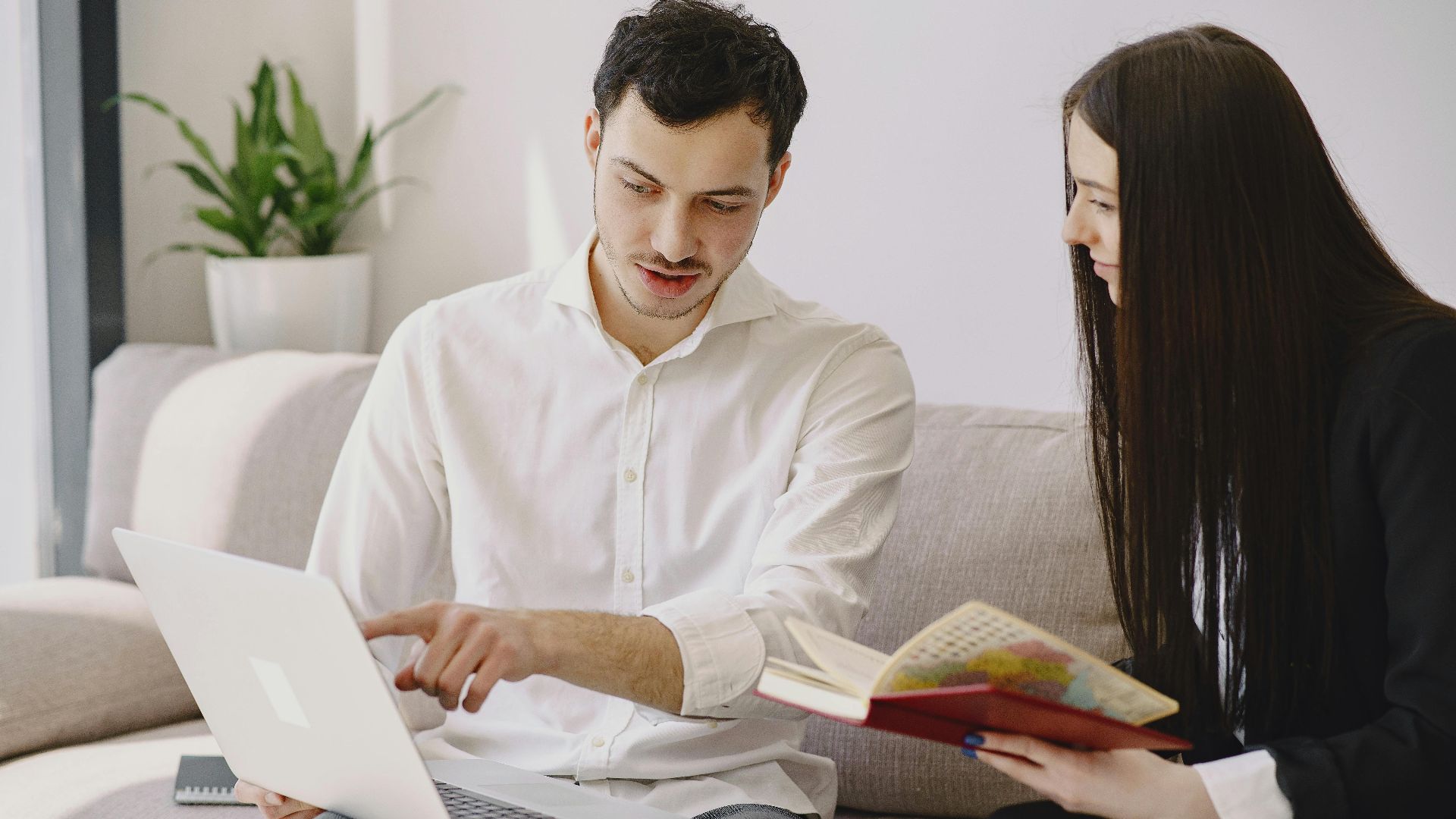 Colleagues collaborating indoors with a laptop and a notebook in a casual office setting.
